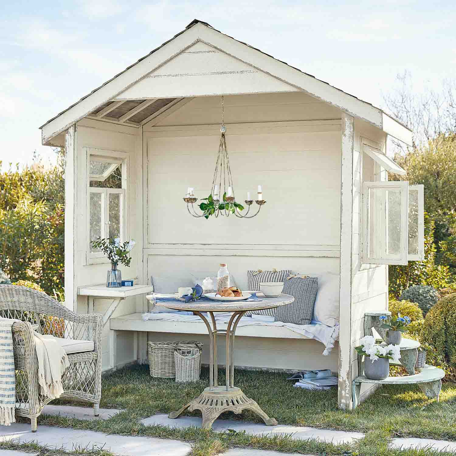 Weißes Holz-Gartenhaus mit Korbsessel und rundem Tisch auf Rasenfläche