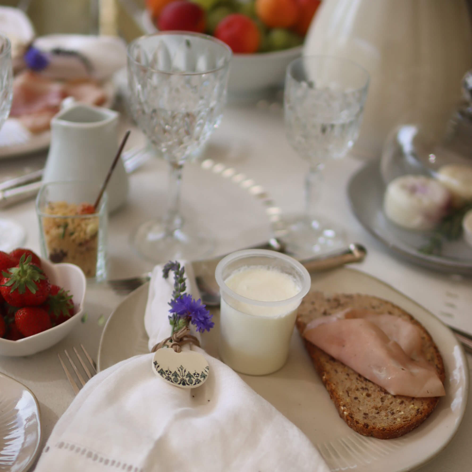 Frühstückstisch mit Vollkornbrot, Schinken und Joghurt auf Teller, Serviette mit Blumendekor
