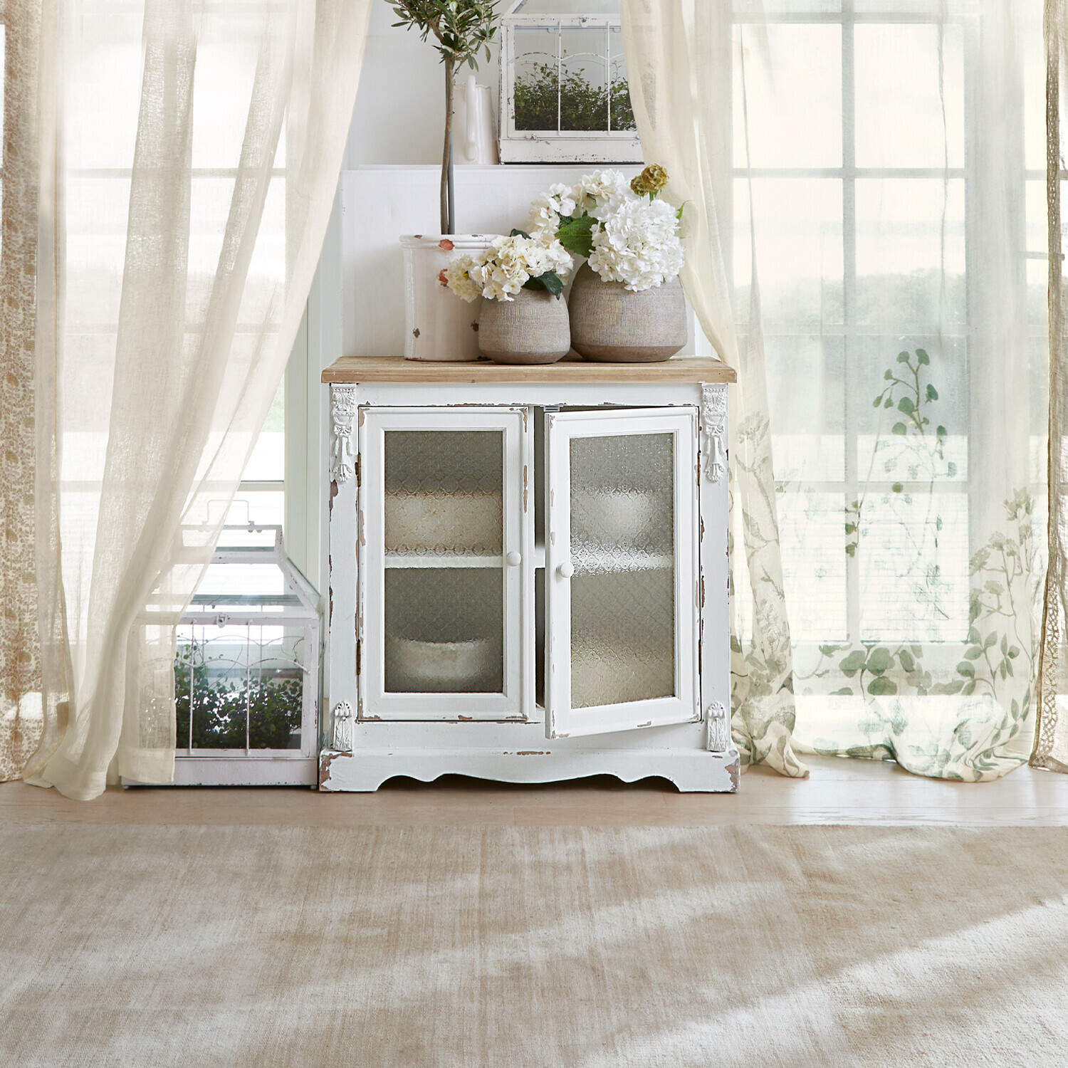 Kommode South Yarmouth Weißer Holzschrank mit Glastüren und dekorativen Blumenvasen in hellem Raum