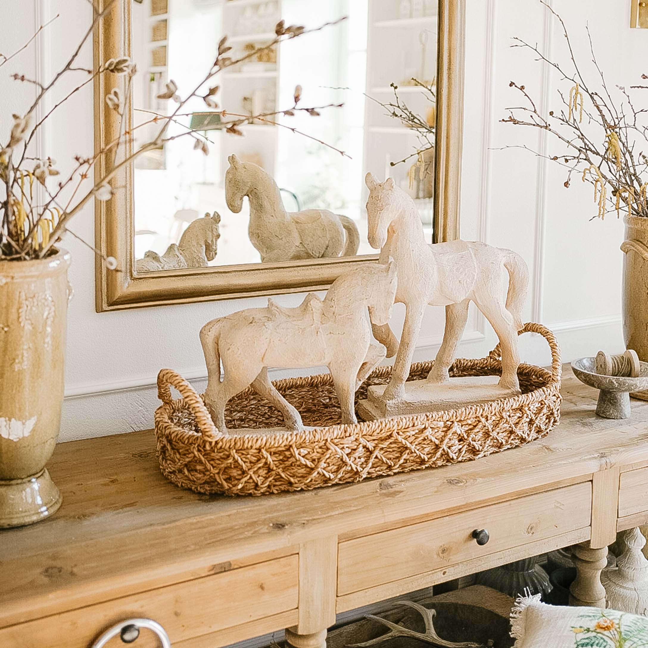 Weiße Pferdefiguren aus Material auf geflochtenem braunem Tablett auf Holztisch dekorativ