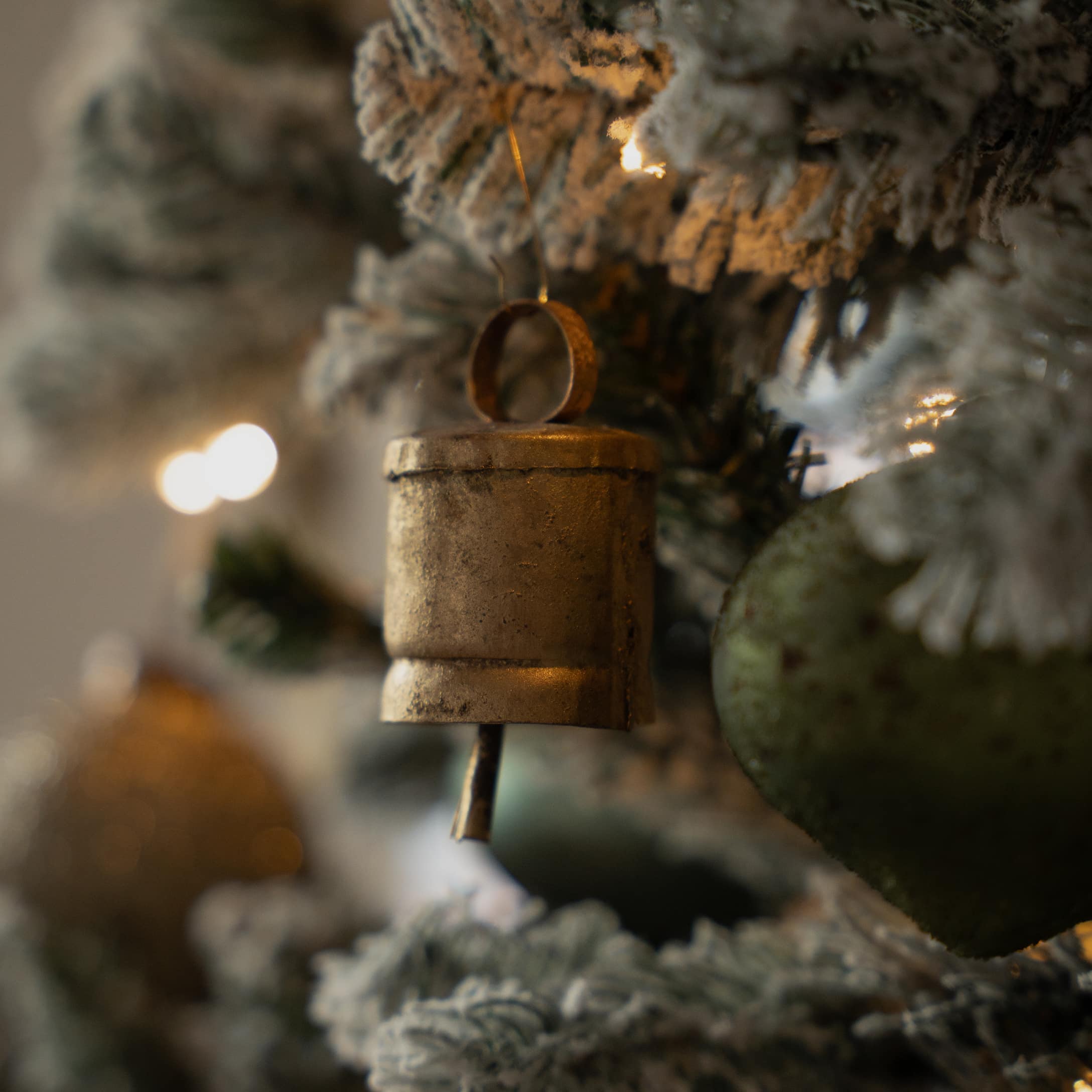 Goldener Metallglöckchen-Anhänger an schneebedecktem Weihnachtsbaum mit Herzdeko