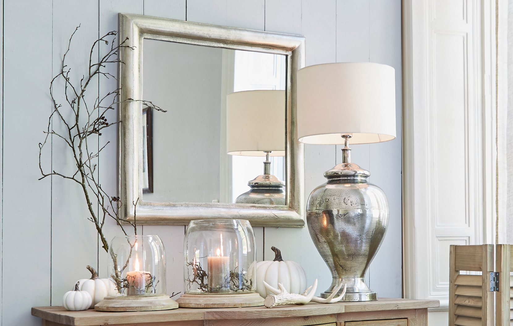 Klassisch elegantes Interieur mit silbernem Spiegel, Metalllampe und Dekorationen auf Holzkommode