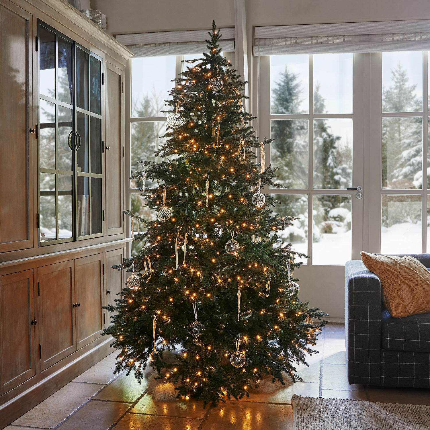 Weihnachtsbaum Celindor Beleuchteter Weihnachtsbaum mit grünen Zweigen und gläsernen Kugeln in gemütlichem Wohnzimmer mit Schneeblick