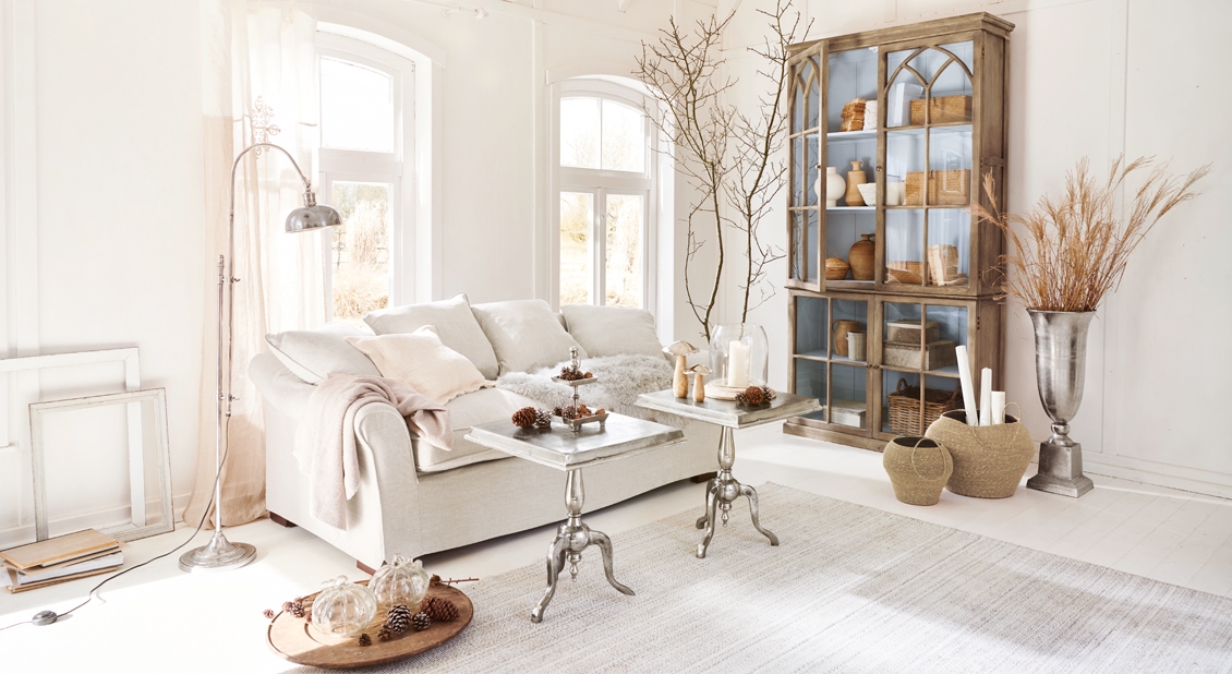 Helles Wohnzimmer mit beigem Sofa, Metalltischen und rustikalem Holzvitrinenschrank