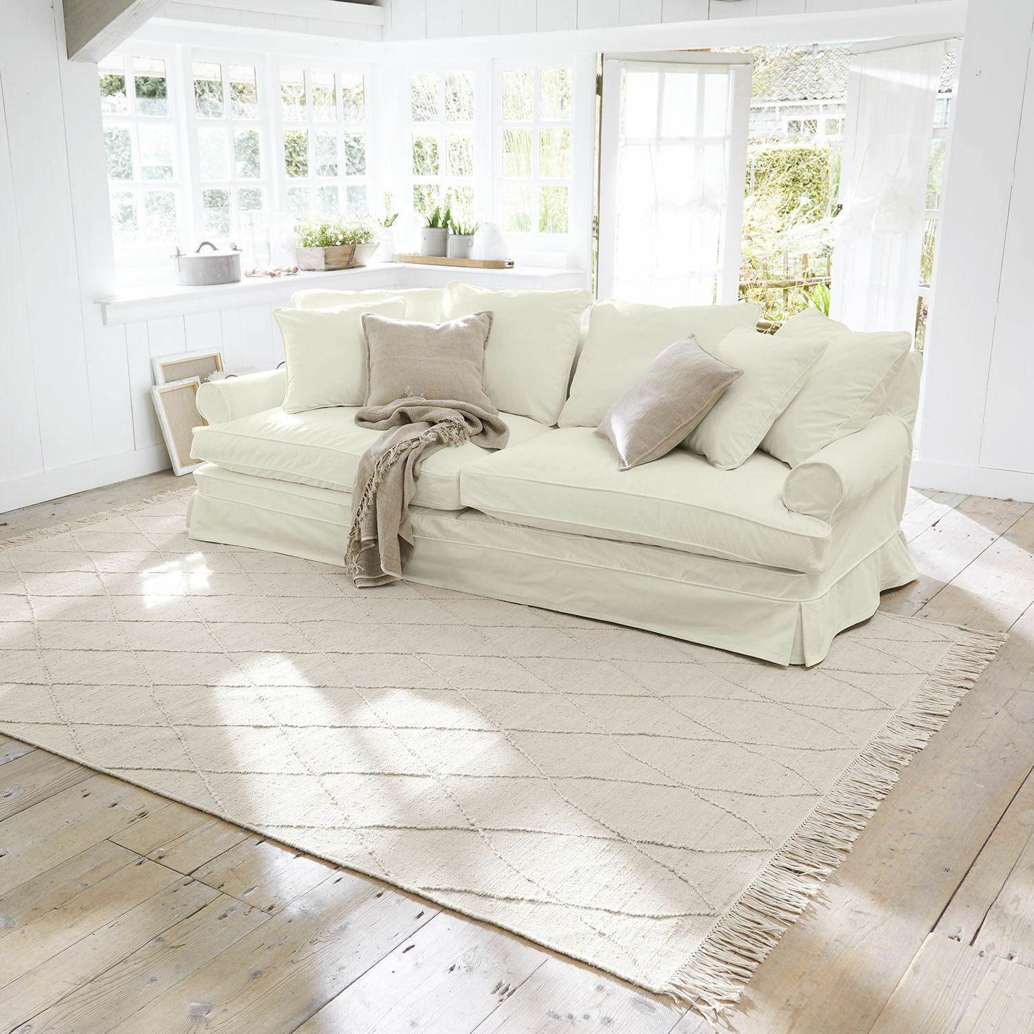 Teppich Ivonique Beige helles Sofa mit weichen Kissen und Decke in hellem, gemütlichem Wohnzimmer
