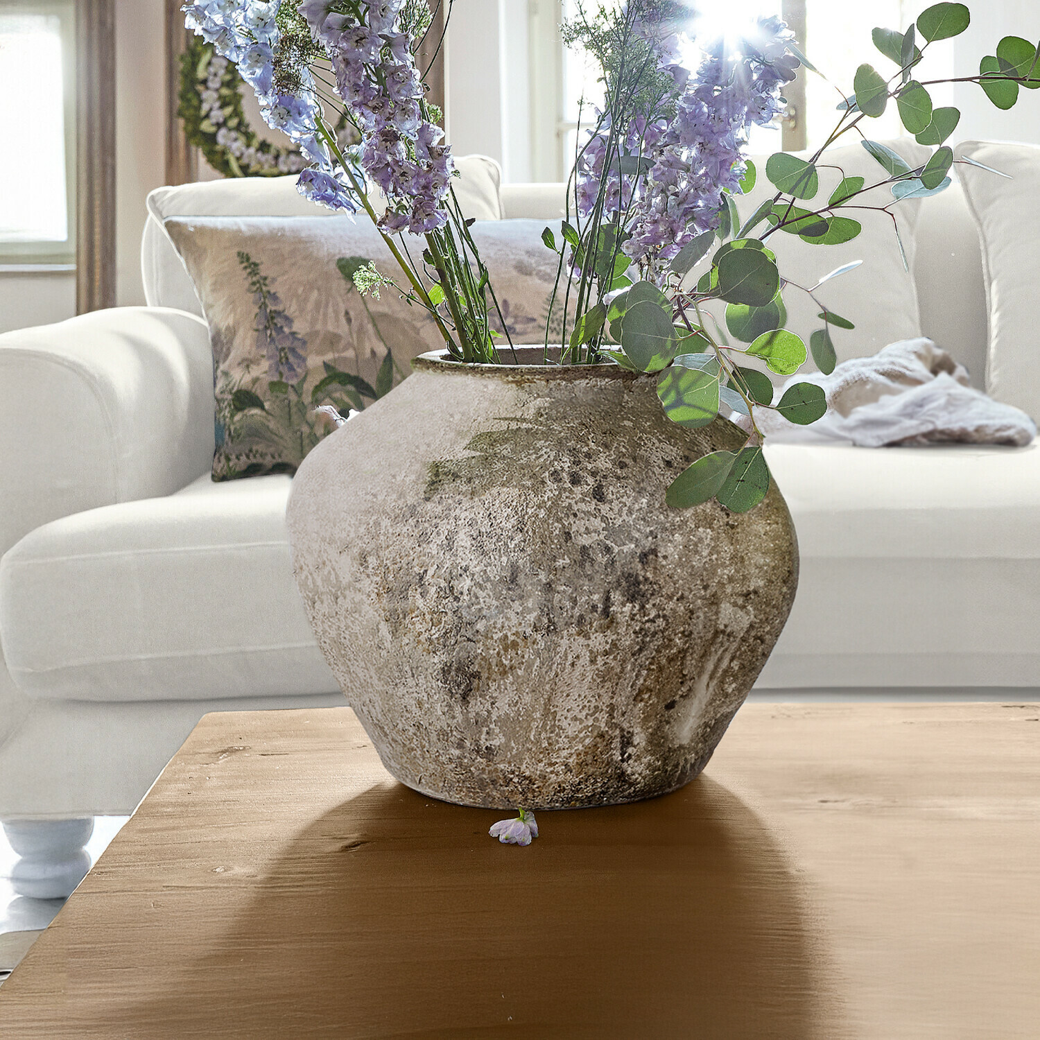 Große Keramikvase in Naturfarbe mit lila Blumen auf Holztisch in hellem Wohnzimmer