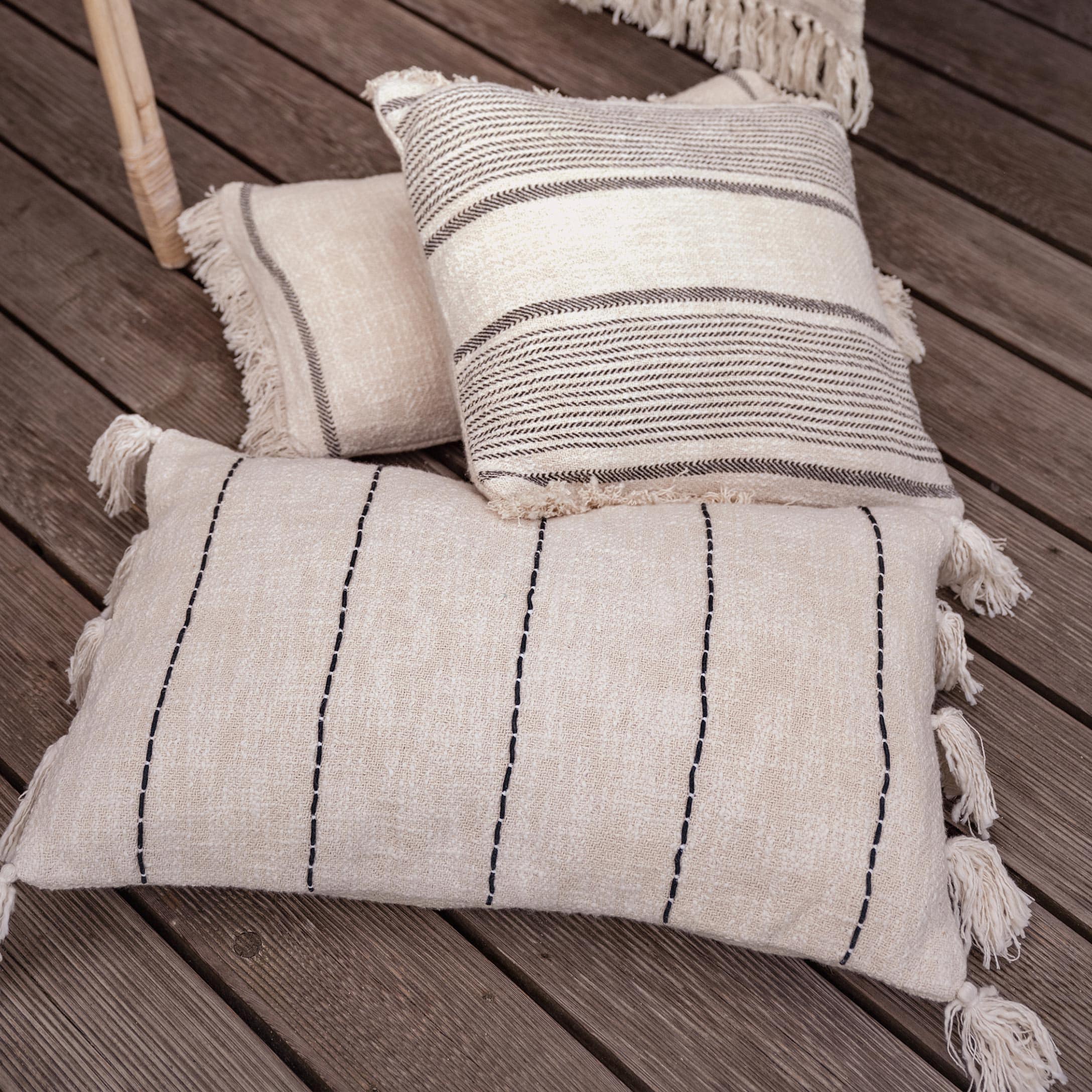 Beige Baumwoll-Dekokissen mit Fransen und Mustern auf Holzboden, Boho-Stil Wohnaccessoire