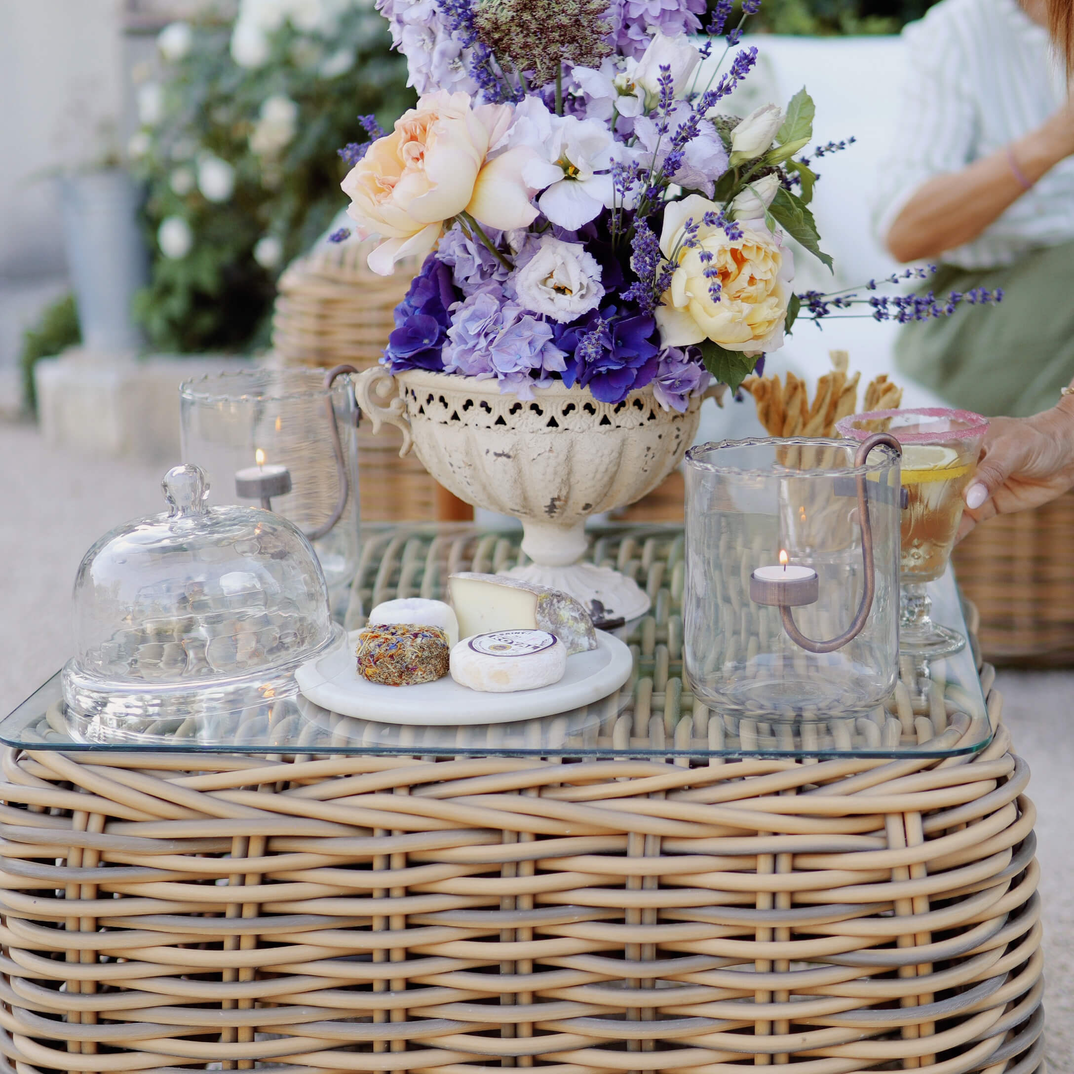 Dekorativer Lavendel- und Rosenstrauß in weißer Keramikvase auf Rattantisch mit Glas und Käse