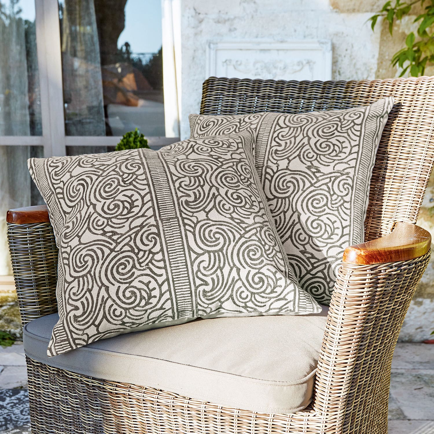 Kissenhülle 2er Set Ensis Zwei dekorative Baumwollkissen in Beige mit braunem Muster auf Rattansessel auf Terrasse