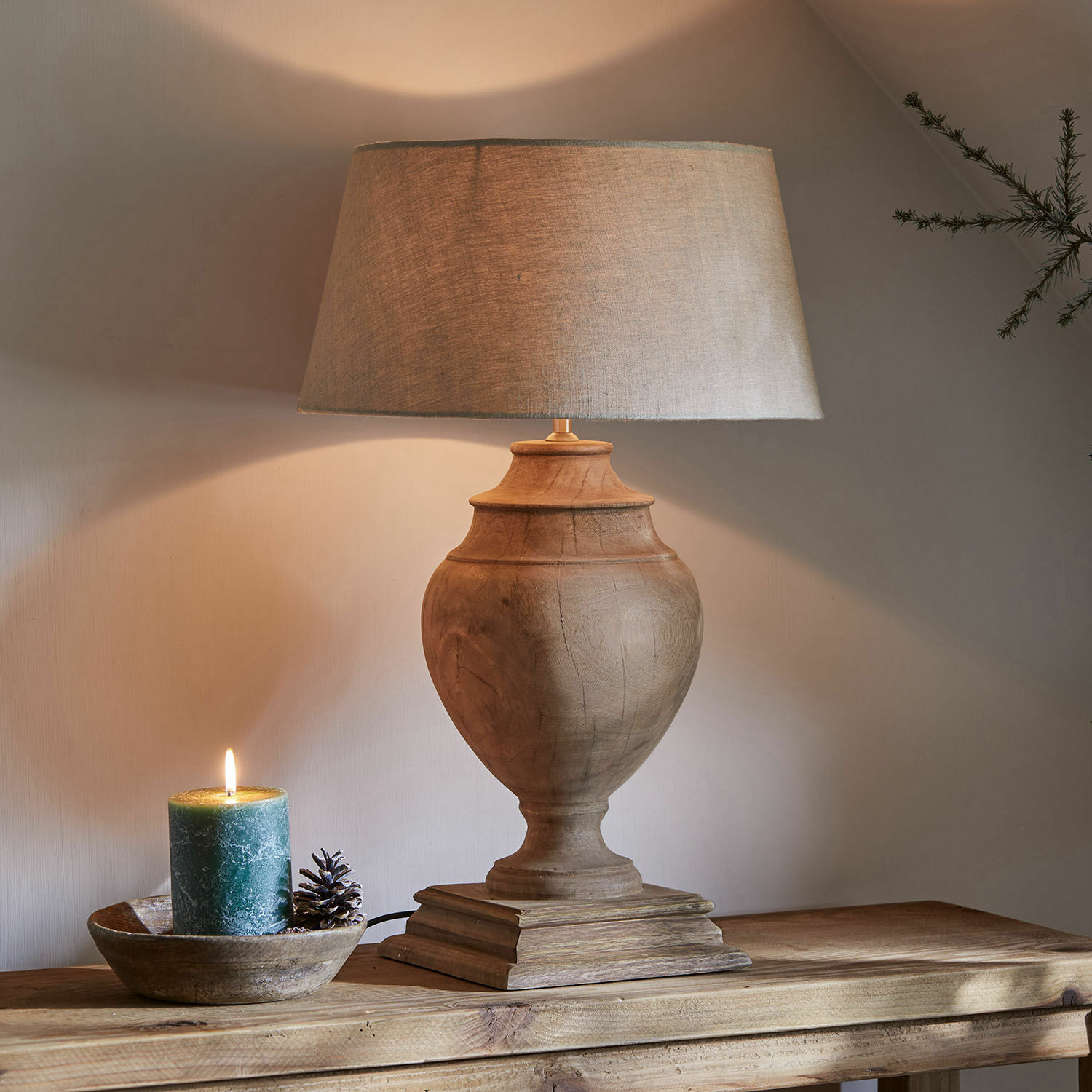 Tischlampe Sauverny Tischlampe mit Holzfuß und beigem Lampenschirm auf Holztisch, daneben dekorative Kerze