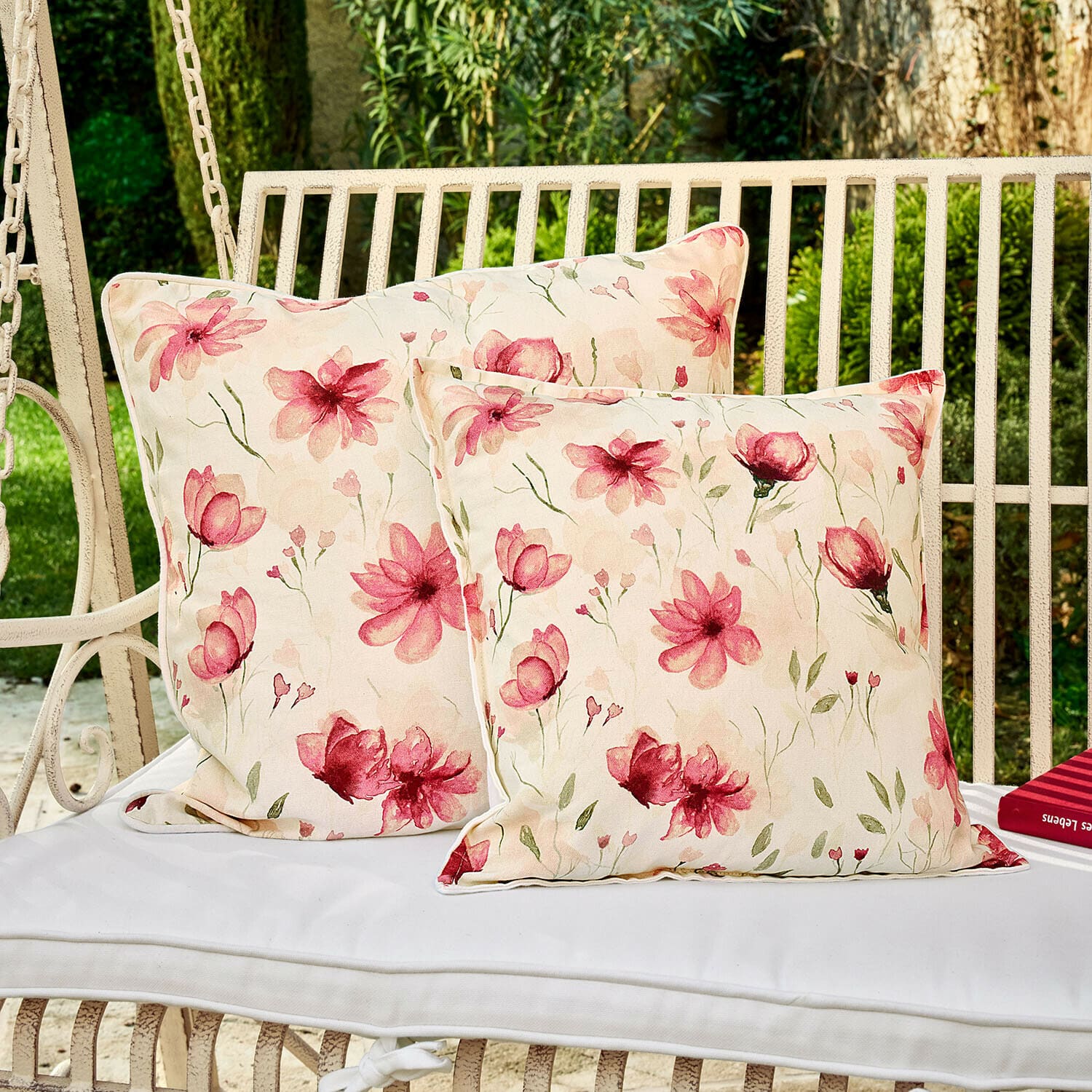 Zwei dekorative Kissen mit floralem Muster auf weißer Gartenschaukel, Baumwollstoff, hellrosa Blumen