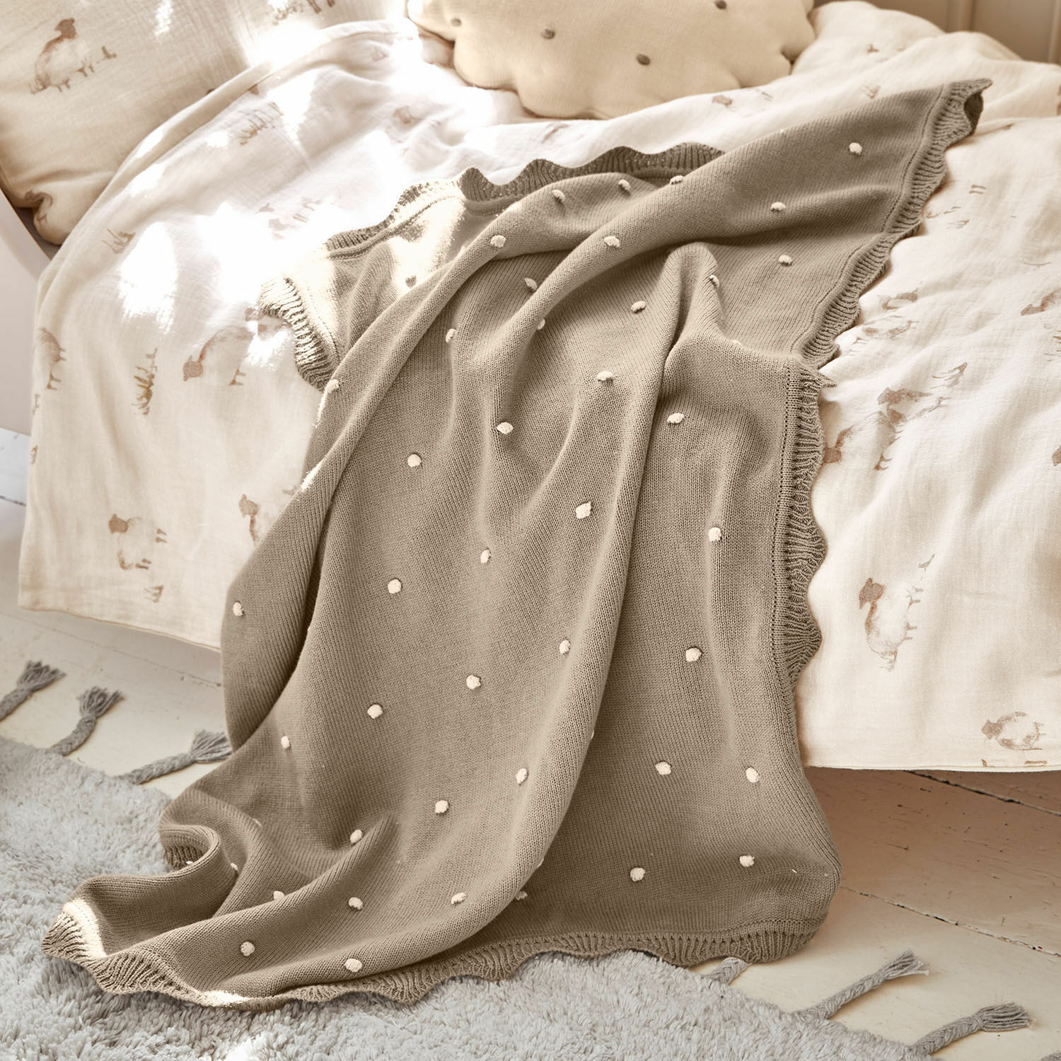 Beige gestrickte Decke mit weißen Punkten auf hellem Bett, weiche und dekorative Wohndecke