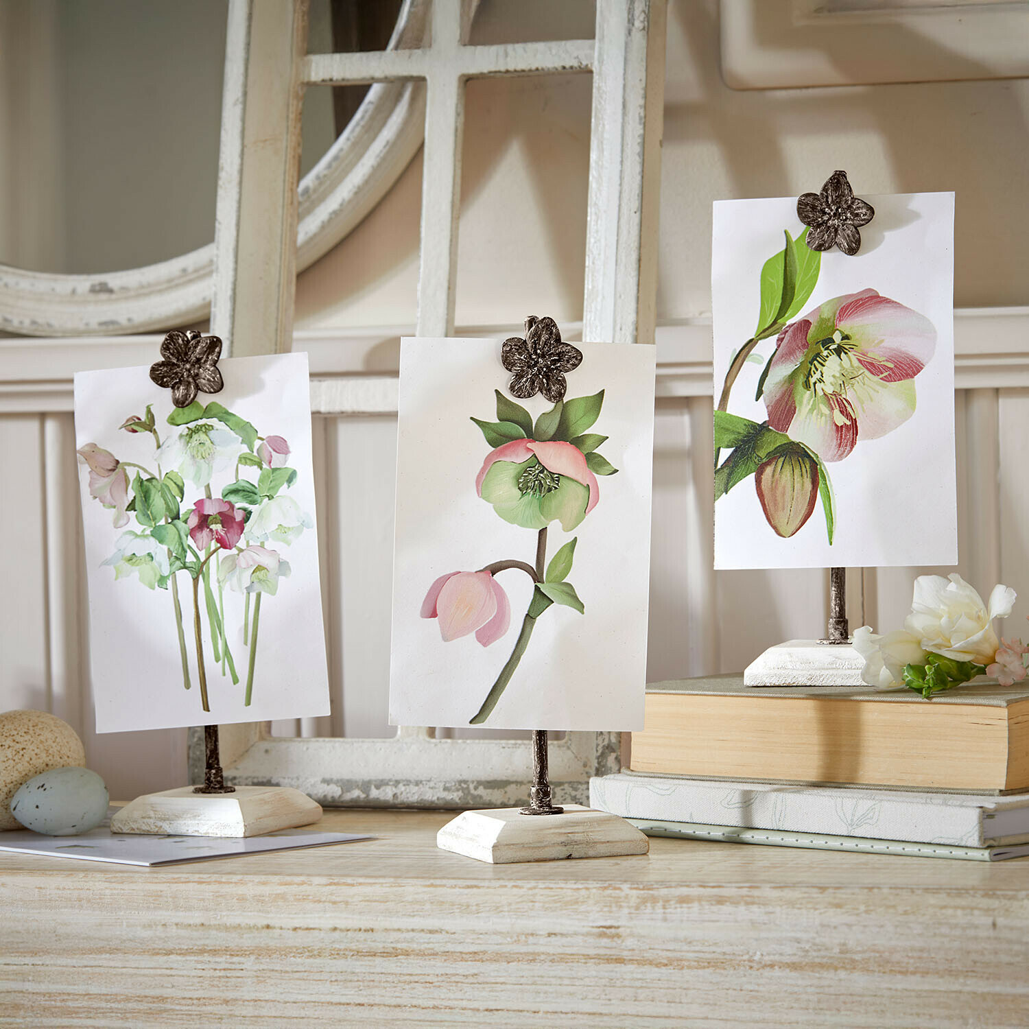 Drei weiße Holz-Fotohalter mit metallischen Blumenklammern als Tischdekoration im Vintage-Stil
