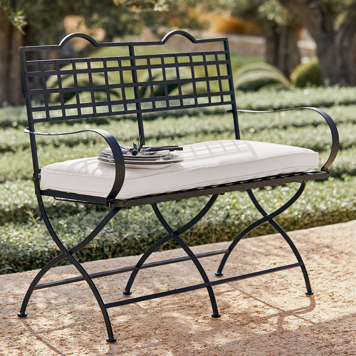 Bank Terell Schwarze Metall-Gartenbank mit weißem Sitzkissen auf steinerner Terrasse im Freien