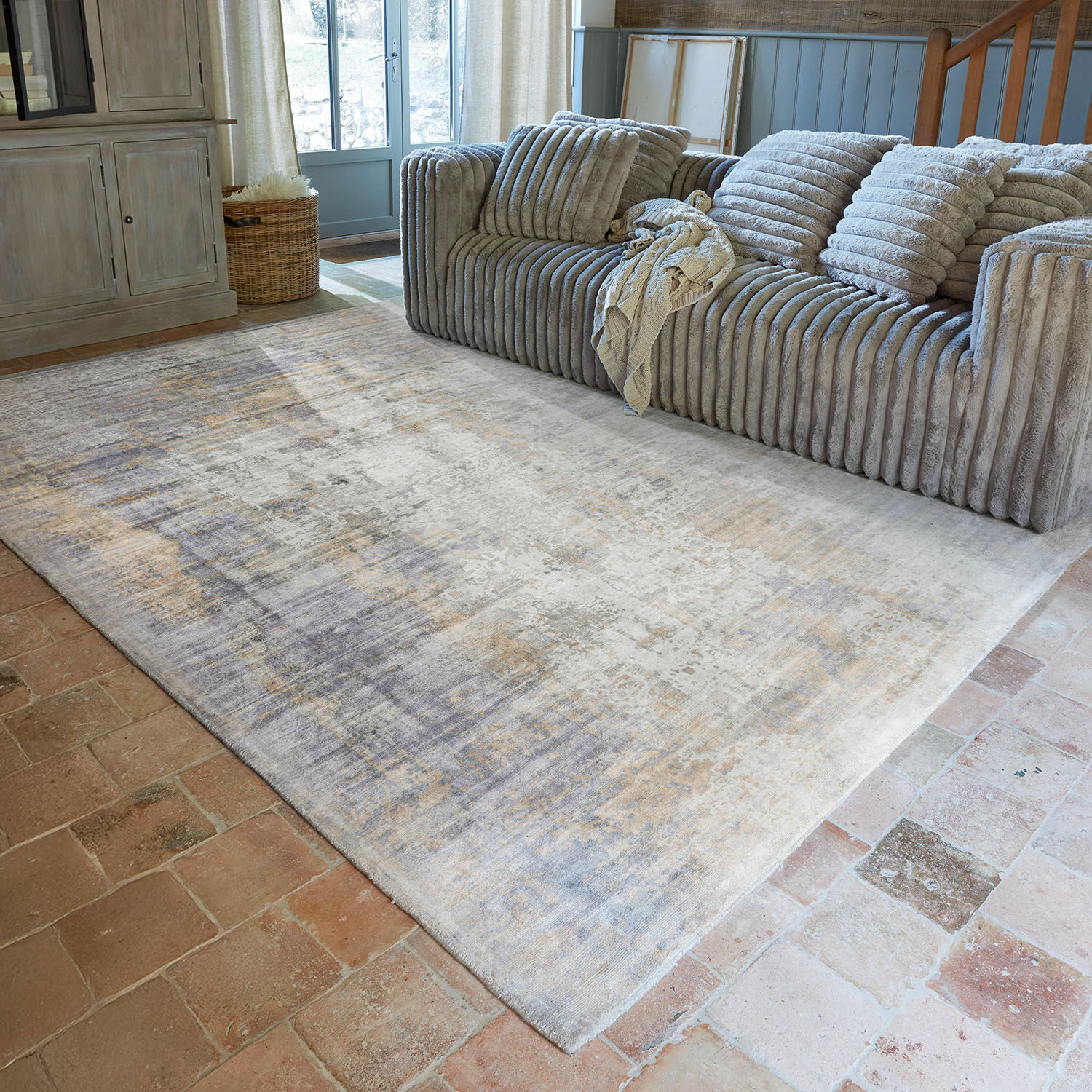 Teppich Qalheera Großer Teppich in Grau- und Beigetönen auf Ziegelboden vor grauem Sofa im Wohnzimmer