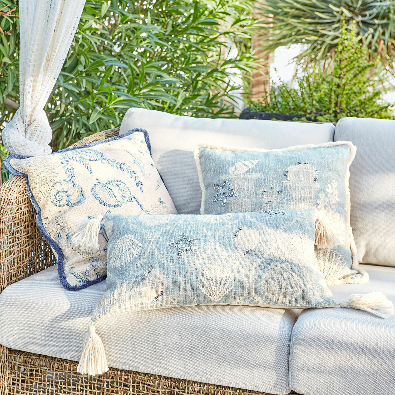 Kissenhülle 3er Set Calerand Dekorative Kissen mit Muschel- und Seesternmotiven in Blau- und Beigetönen auf Rattansofa