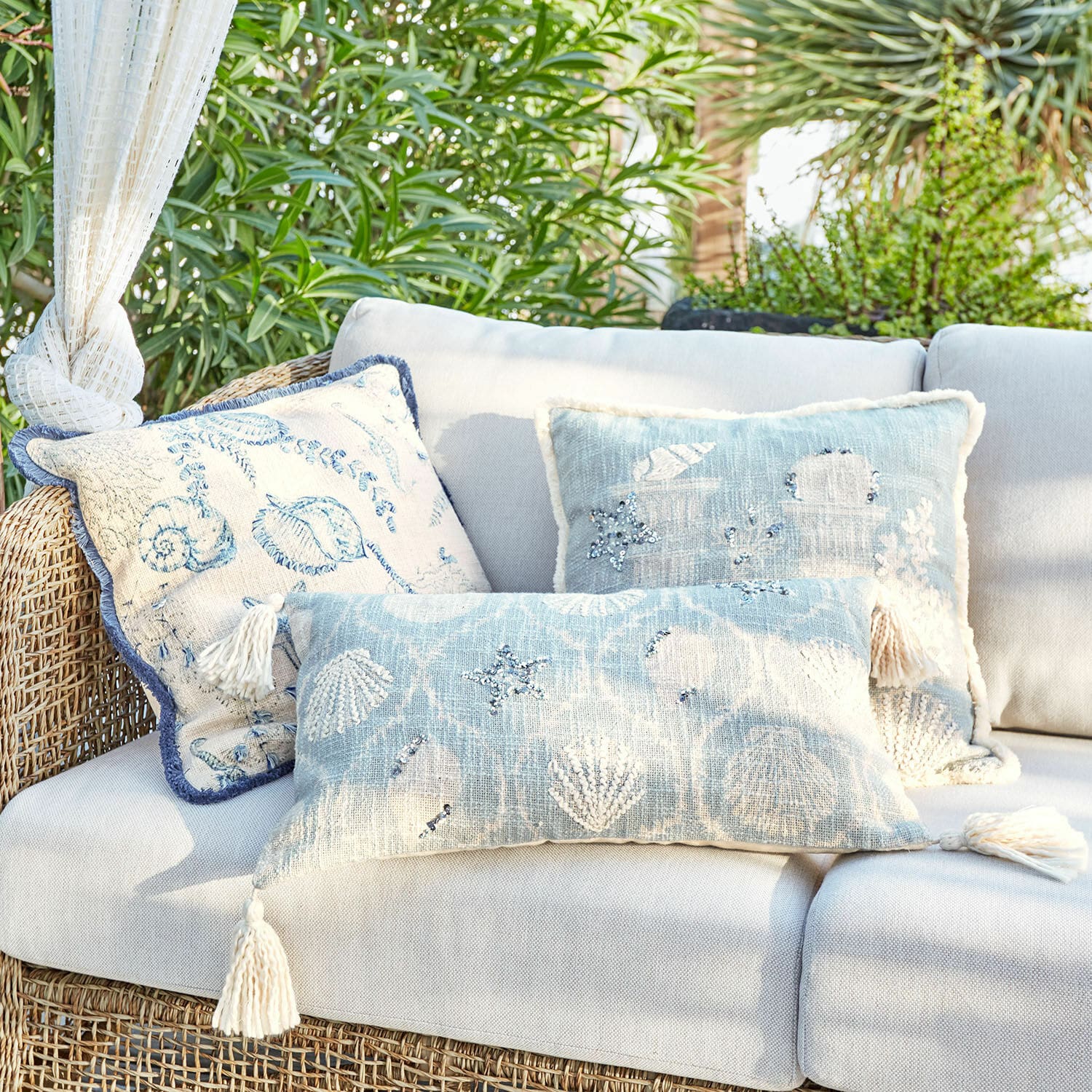 Kissenhülle 3er Set Calerand Dekorative Kissen mit Muschel- und Seesternmotiven in Blau- und Beigetönen auf Rattansofa