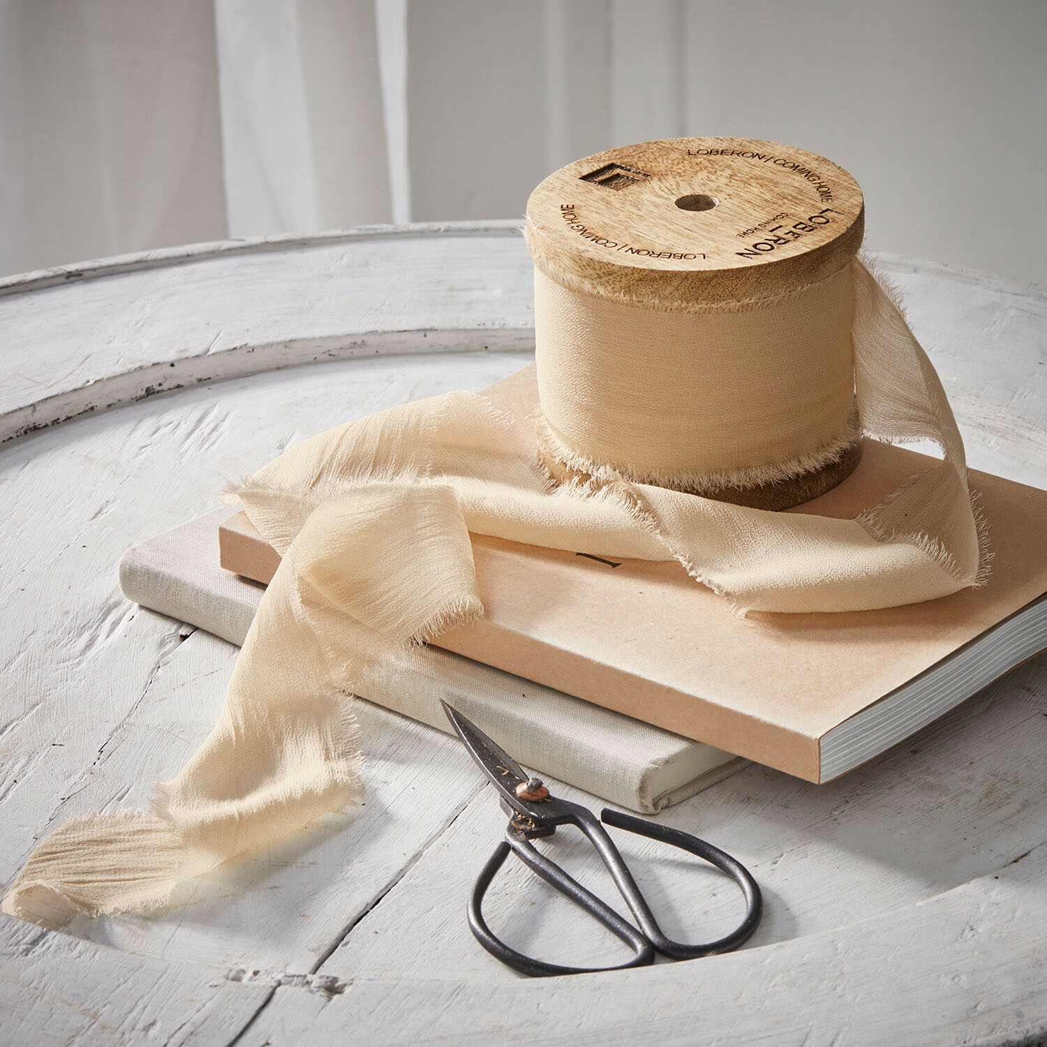 Beige Fransenband auf Holzspule mit Schere auf weißem Tisch für Dekoration und Bastelarbeiten