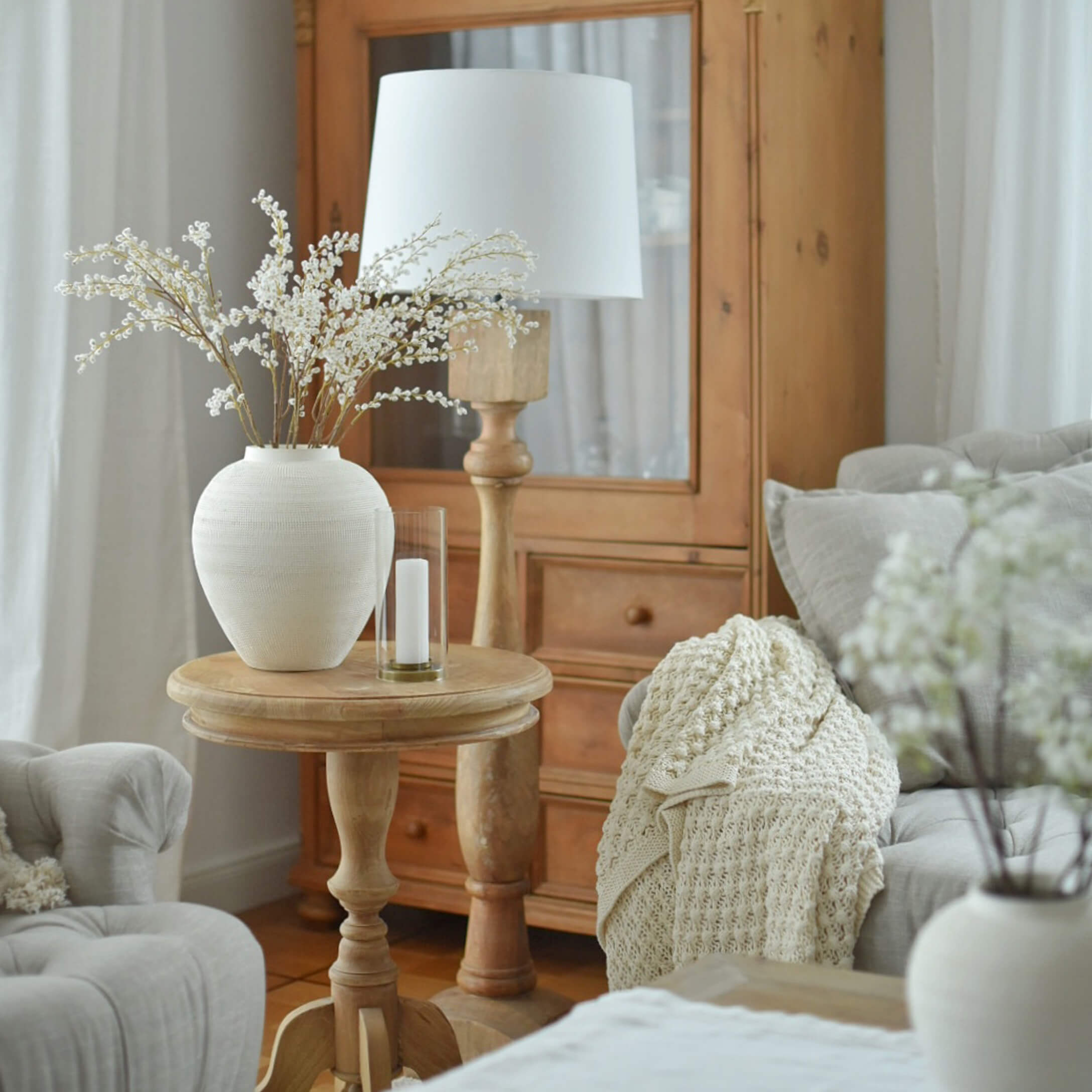 Heller Holztisch mit weißer Keramikvase und Lampe in gemütlichem Wohnzimmer mit beiger Decke