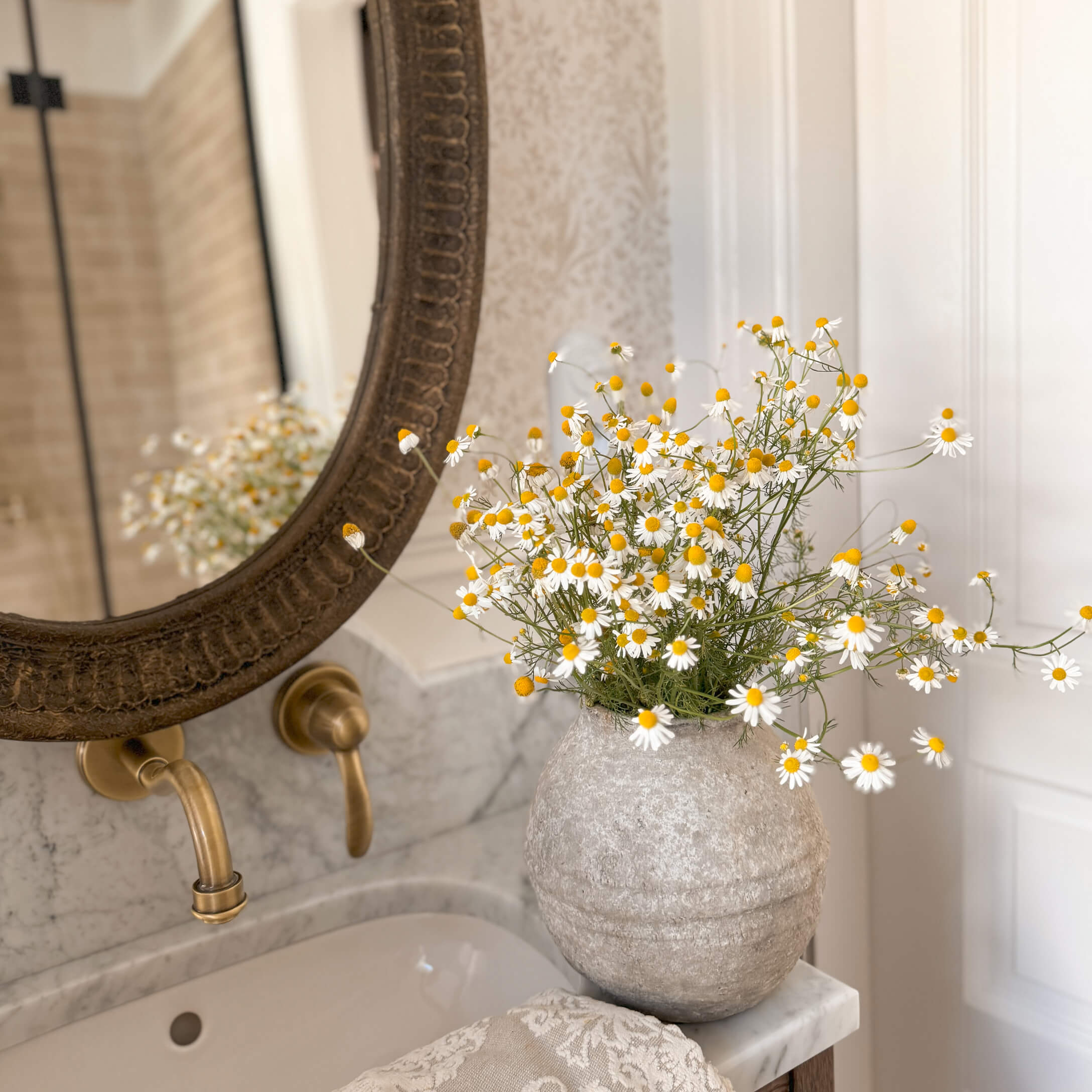 Grauer Steinvase mit weißen und gelben Blumen auf Marmorwaschbecken in stilvollem Badezimmer