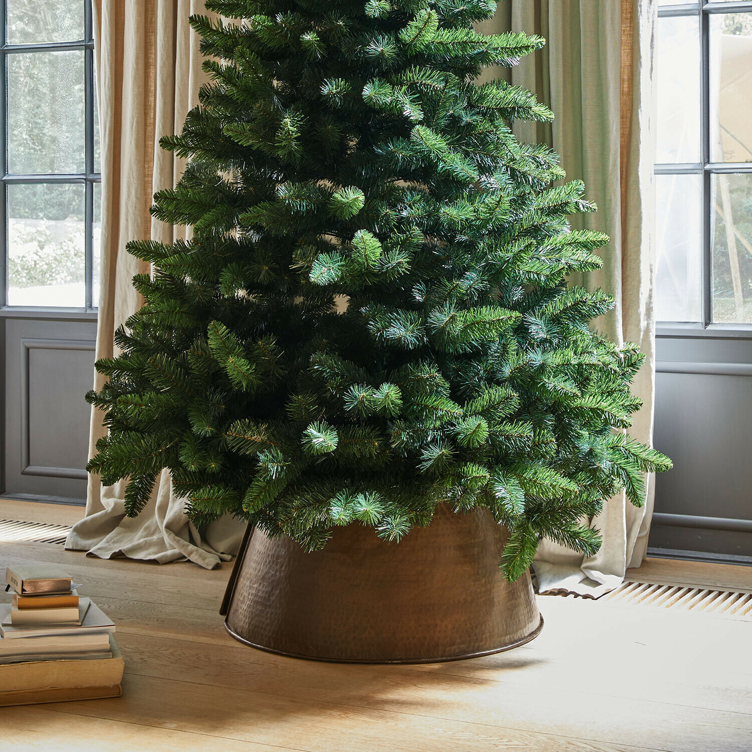Weihnachtsbaumumrandung Omeyra Künstlicher Weihnachtsbaum in kupferfarbenem Metallübertopf auf hellem Holzboden neben Büchern