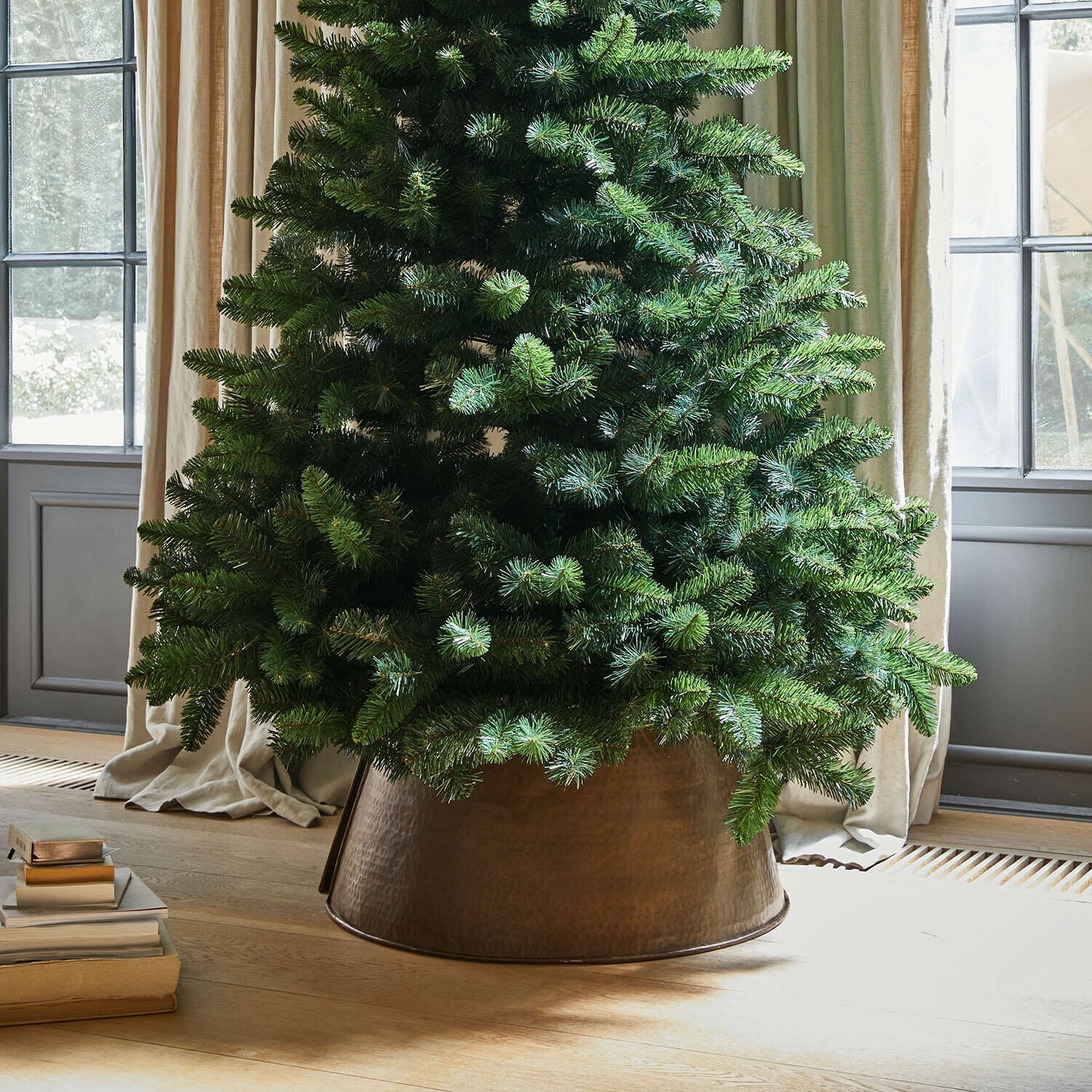 Weihnachtsbaumumrandung Omeyra Künstlicher Weihnachtsbaum in kupferfarbenem Metallübertopf auf hellem Holzboden neben Büchern