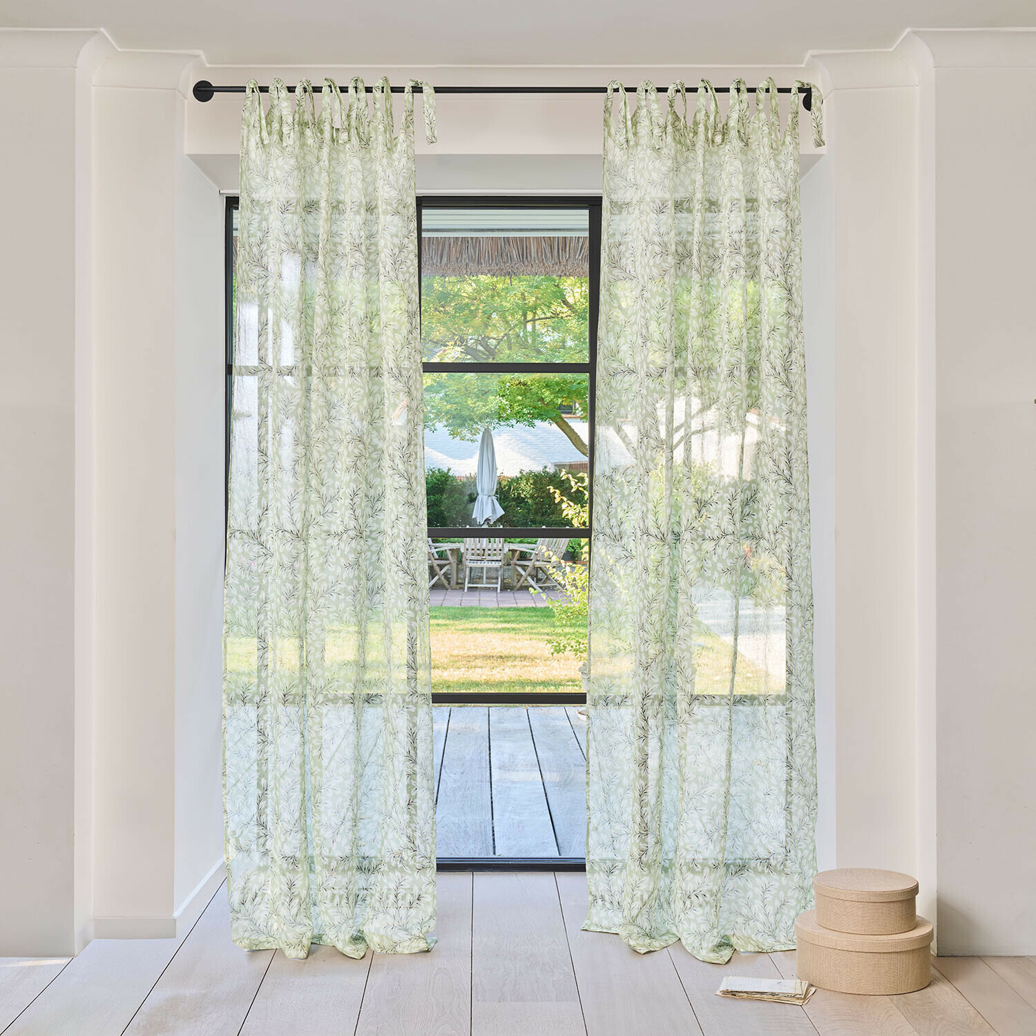 Transparente Vorhänge mit grünem Blattmuster an schwarzem Vorhangstange in hellem Raum mit Gartenblick