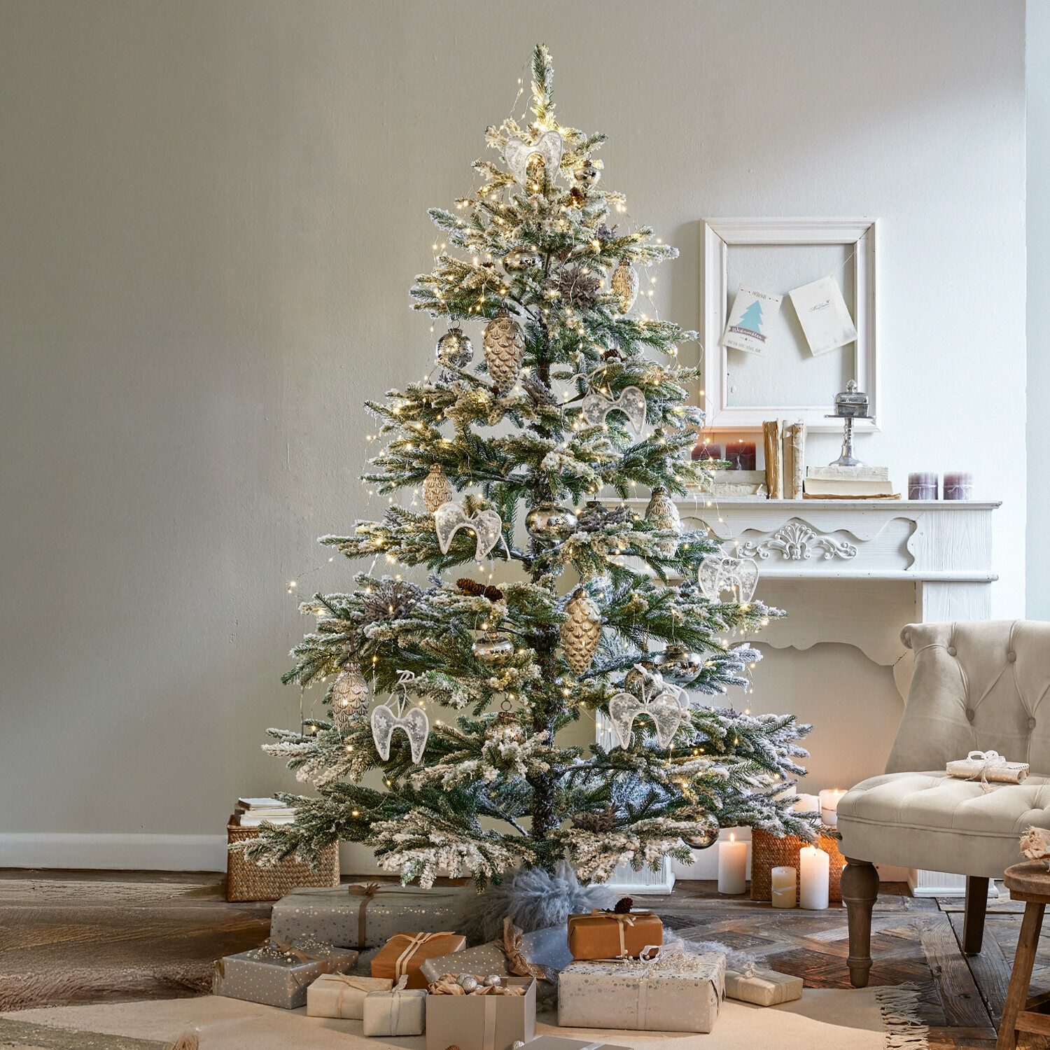 Weihnachtsbaum Lokossa Schneebedeckter Weihnachtsbaum mit weißen und goldenen Dekorationen und Geschenken neben einem beigen Sessel im gemütlichen Wohnzimmer