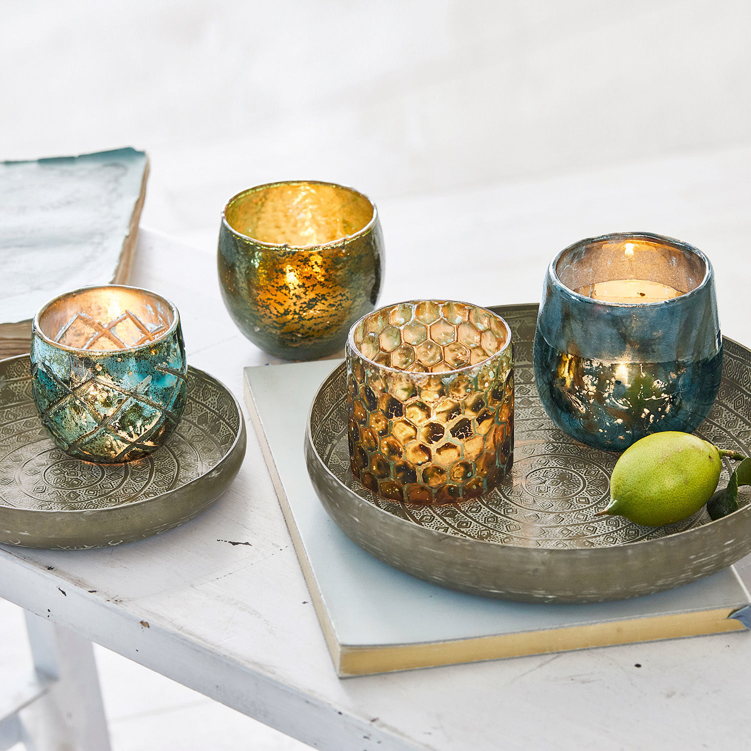 Set aus gold-blauen Glas-Teelichthaltern auf Metalltabletts auf weißem Tisch dekorativ arrangiert