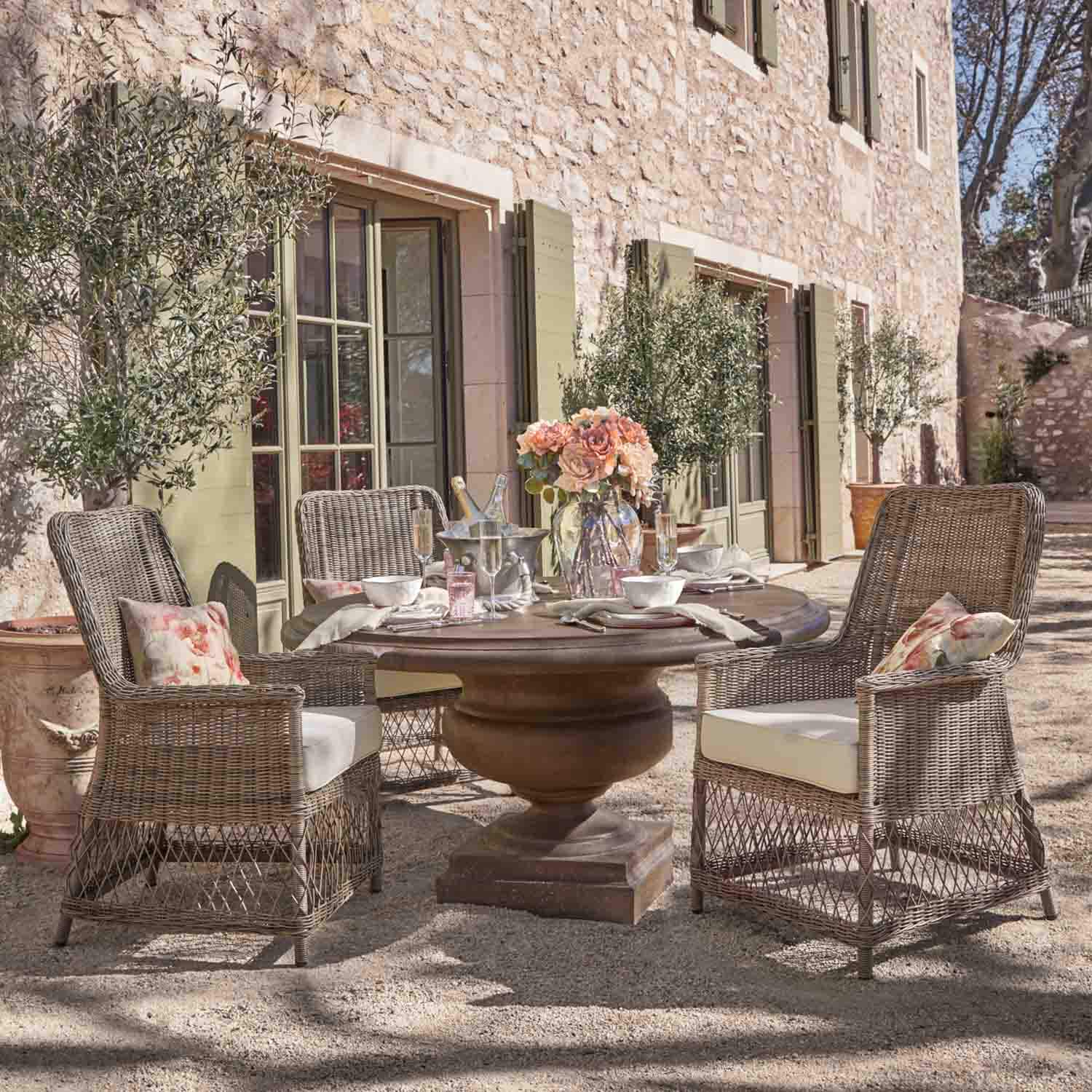 Runder Steintisch mit Rattanstühlen und Blumenarrangement auf sonniger Terrasse im Garten