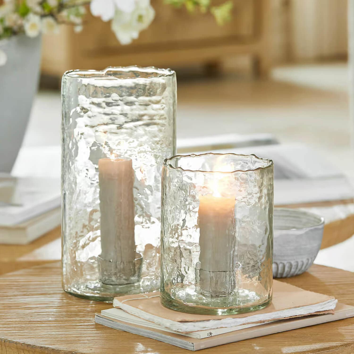 Zwei durchsichtige Glaswindlichter mit weißen Kerzen auf Holztisch, stilvolle Wohnraumdekoration
