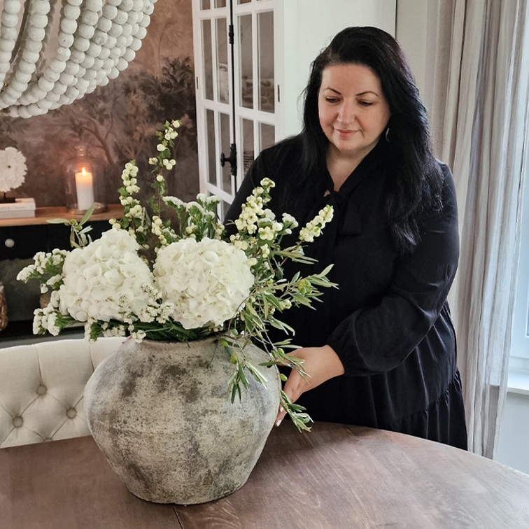 Große graue Keramikvase mit weißen Blumen auf Holztisch in gemütlichem Raum