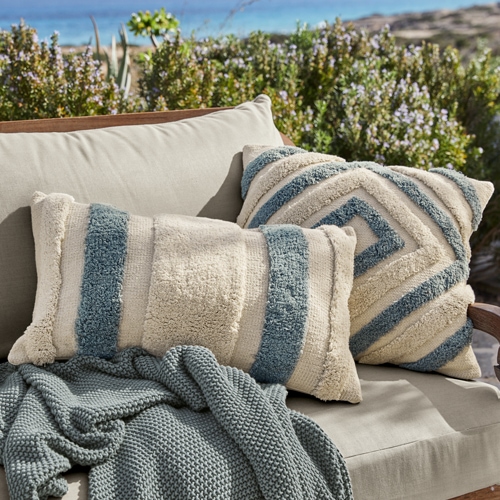 Beige-blaue dekorative Kissen aus weichem Material auf grauem Sofa im Außenbereich, Gartentextilien