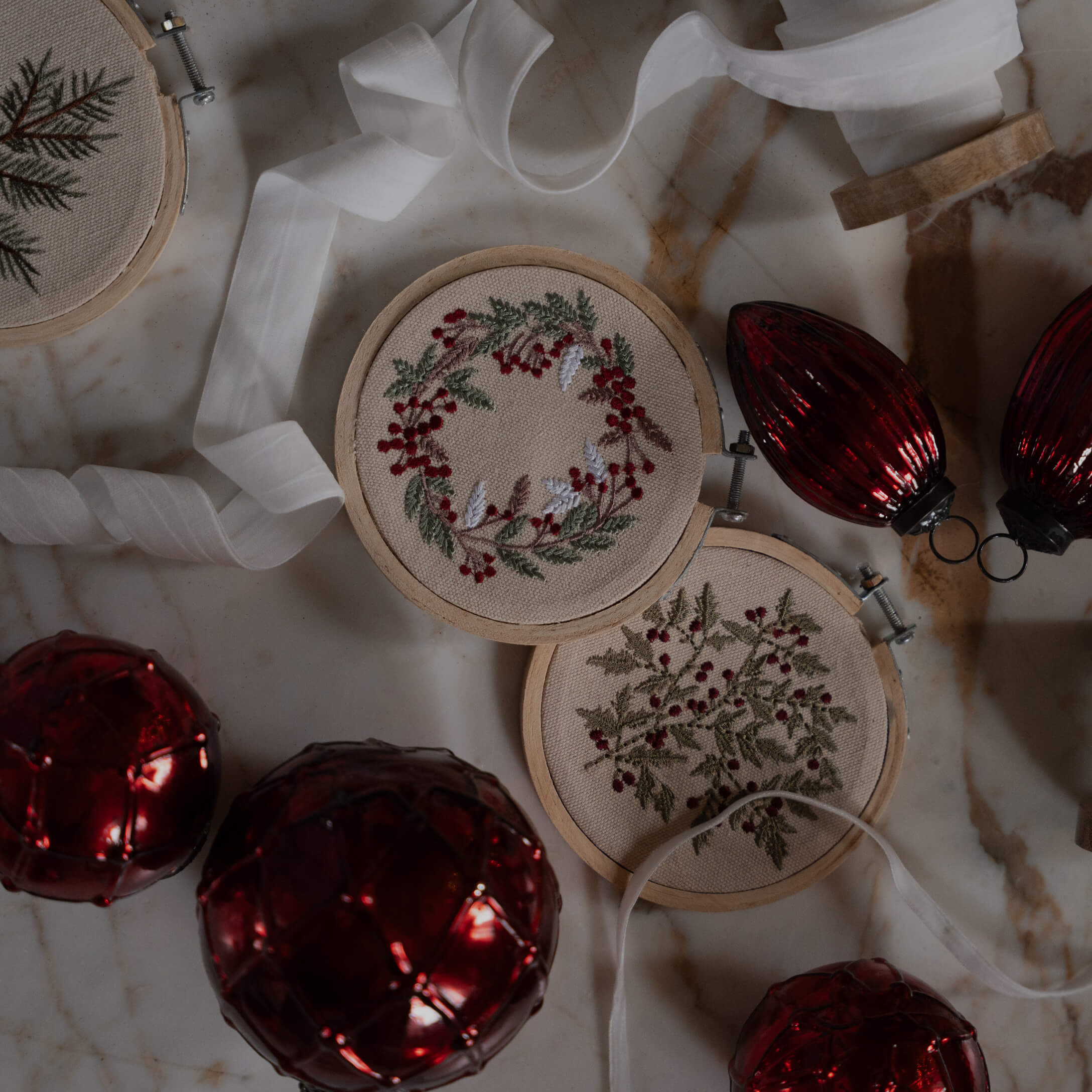 Zwei Stickrahmen mit roten Beeren und grünen Blättern auf beigem Stoff, weihnachtliche Dekoration