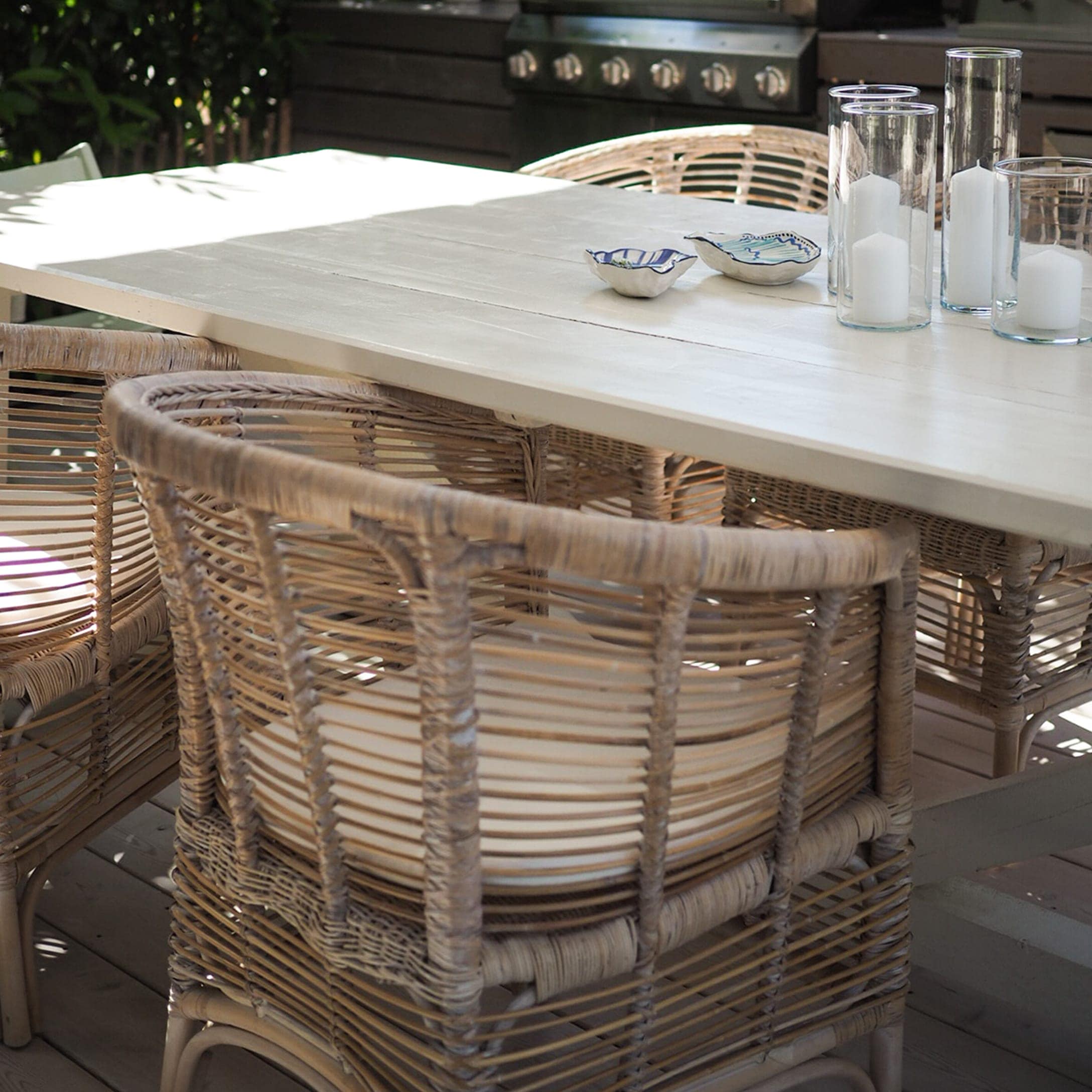 Heller Holztisch mit Rattanstühlen und dekorativen Kerzen auf der Terrasse im Garten