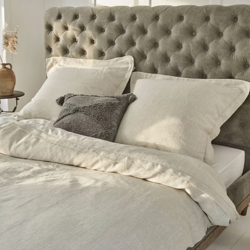 Beige Leinenbettwäsche auf Bett mit grauem, gesteppter Kopfteil, natürliche Stoffe fürs Schlafzimmer