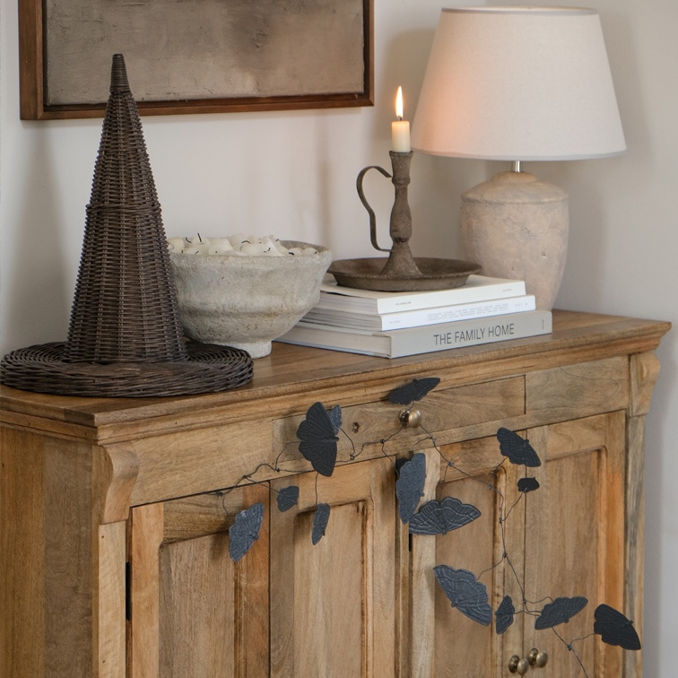 Holzkommode mit schwarzer Blättergirlande, Lampe und Kerzenhalter auf Büchern im Wohnzimmer