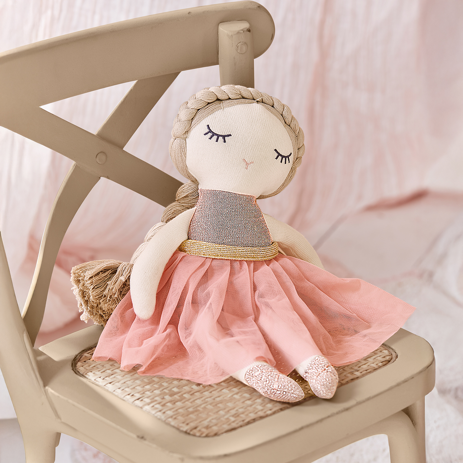 Stoffpuppe mit rosa Kleid und goldenem Gürtel auf beigem Stuhl sitzend, Kinderspielzeug