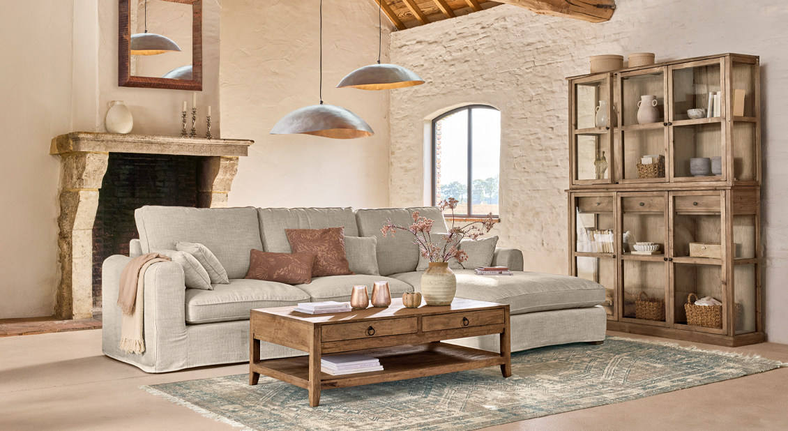 Gemütliches Wohnzimmer mit beigem Sofa, Holztisch und rustikalem Vitrinenschrank aus Naturmaterialien