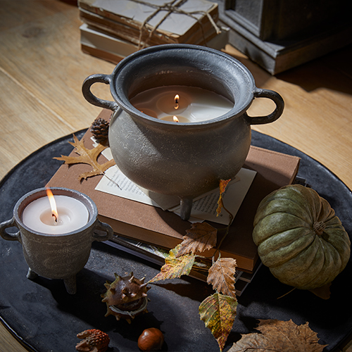 Kerze in grauem Keramiktopf mit Griffen auf Holztisch mit herbstlicher Dekoration