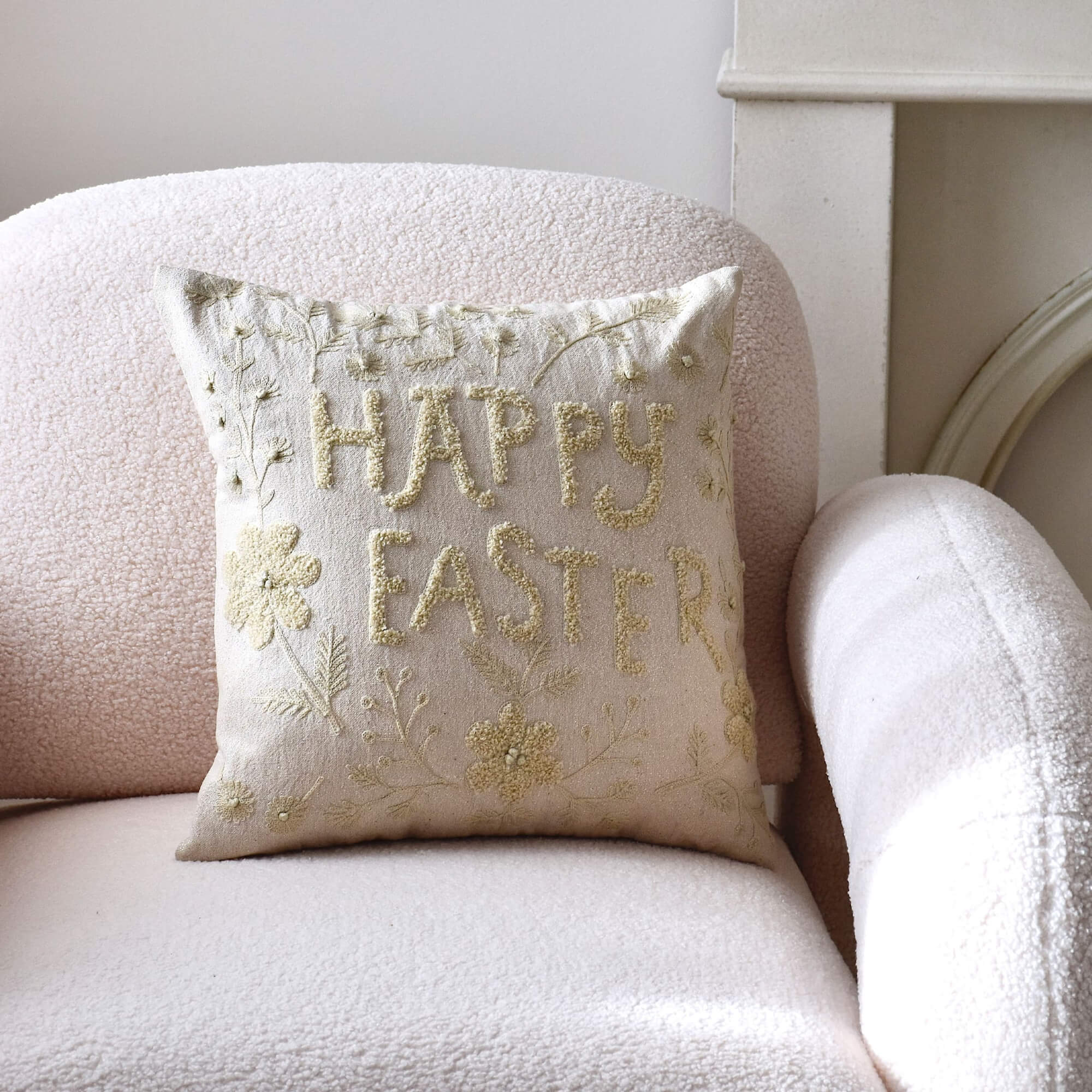 Beige Dekokissen mit Stickerei "Happy Easter" auf hellem Sessel, pastellfarbenes Osterdesign