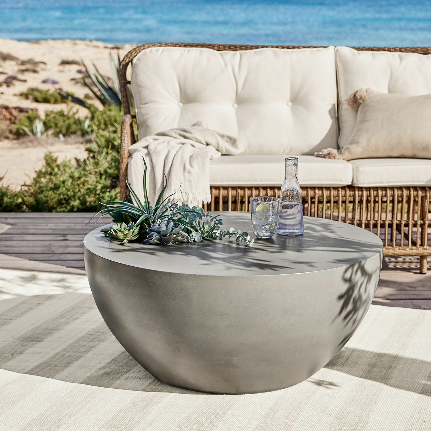 Couchtisch Plévin Runder grauer Couchtisch aus Beton auf Terrasse mit Sukkulenten-Deko und Wasserglas