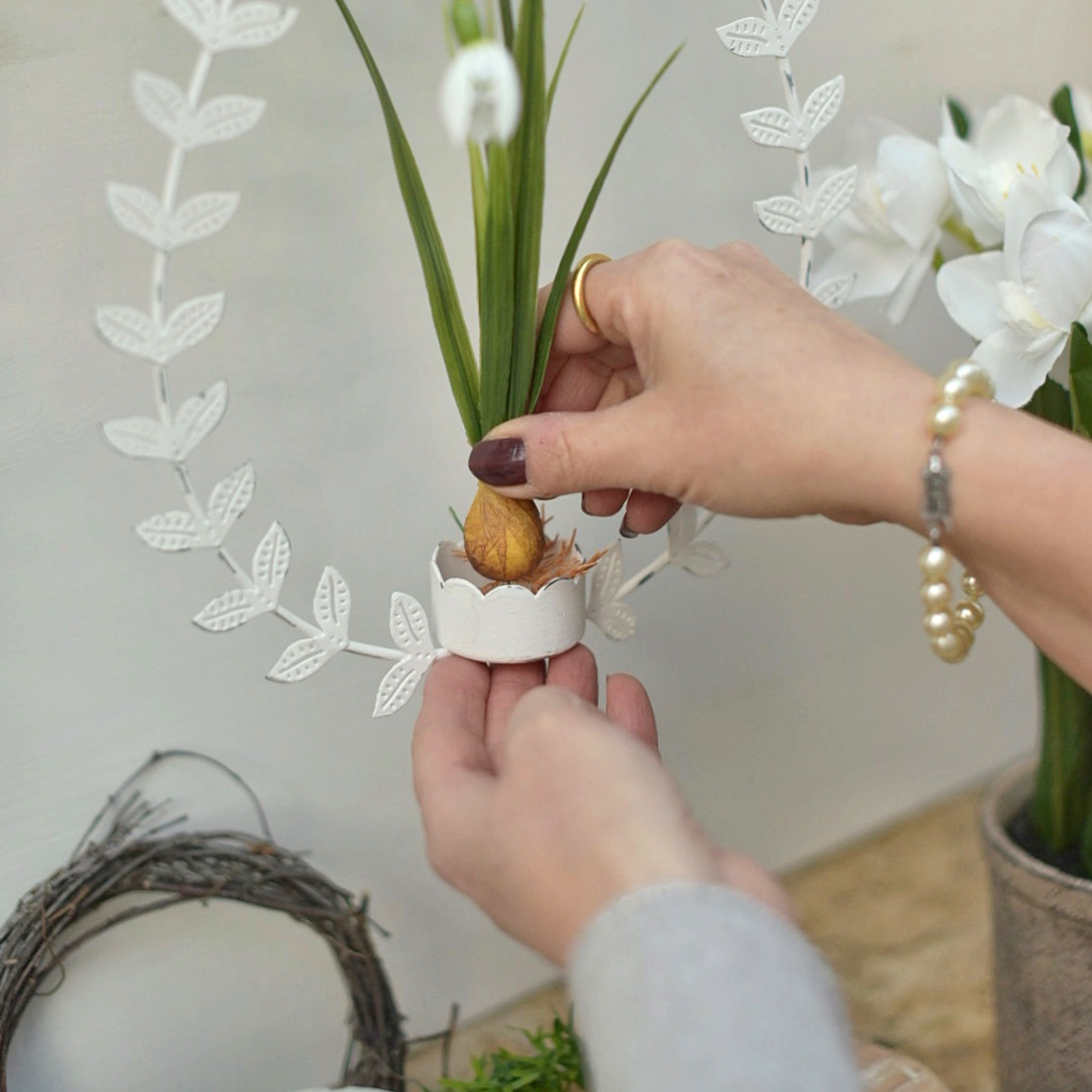 Hände setzen künstliche Blume in weiße Metall-Osterdekoration mit Blättern ein