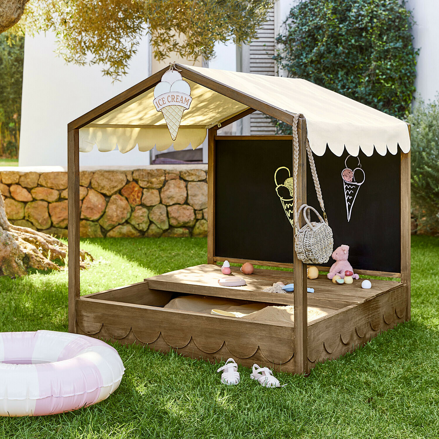 Holz-Sandkasten mit beigem Stoffdach und Tafel, Spielzeug und Eis-Dekorationen im Garten