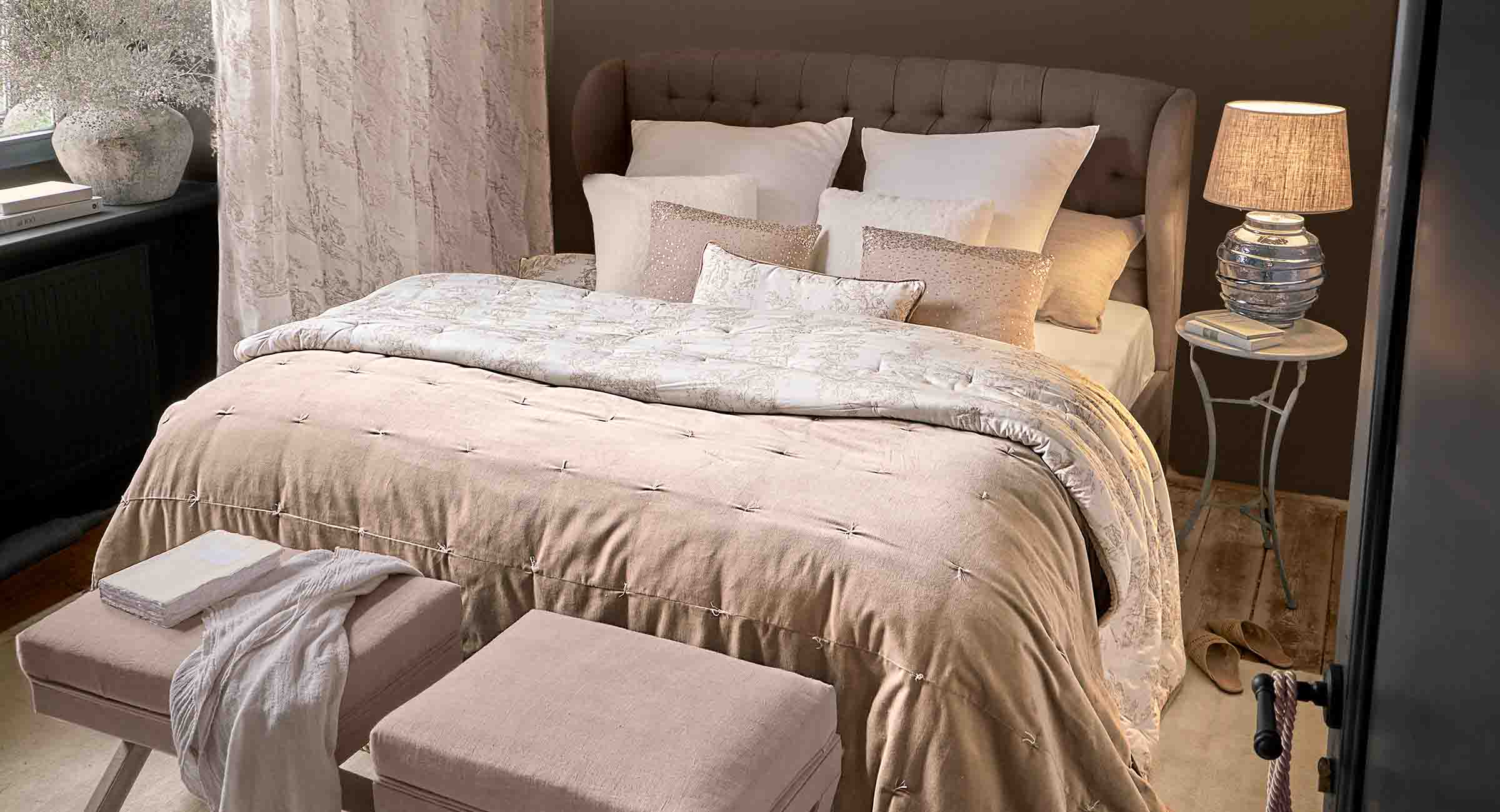 Gemütliches Schlafzimmer mit beiger Bettdecke und Kissen auf gepolstertem Bett, Lampe auf Nachttisch