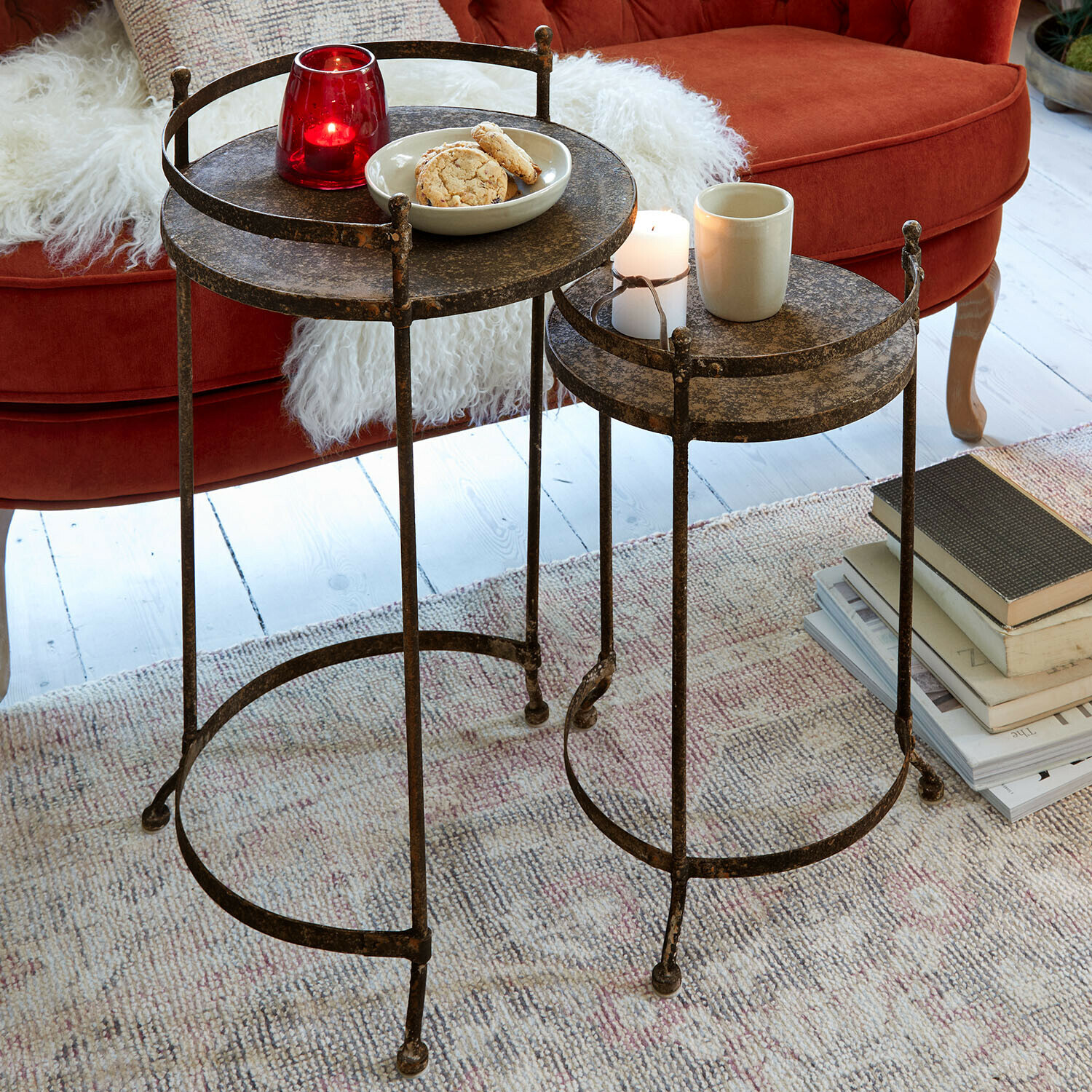 Beistelltisch 2er Set Alanyn Zwei runde Beistelltische aus Metall in antikem Bronze-Finish auf Teppich vor rotem Sofa
