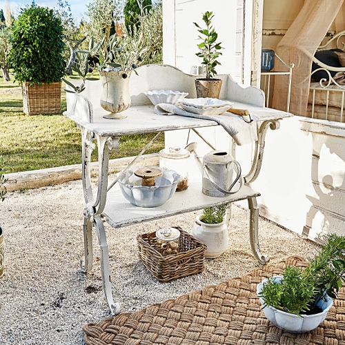 Weißer Metall-Gartentisch im Shabby-Chic-Stil mit Dekorationen und Pflanzen auf der Terrasse