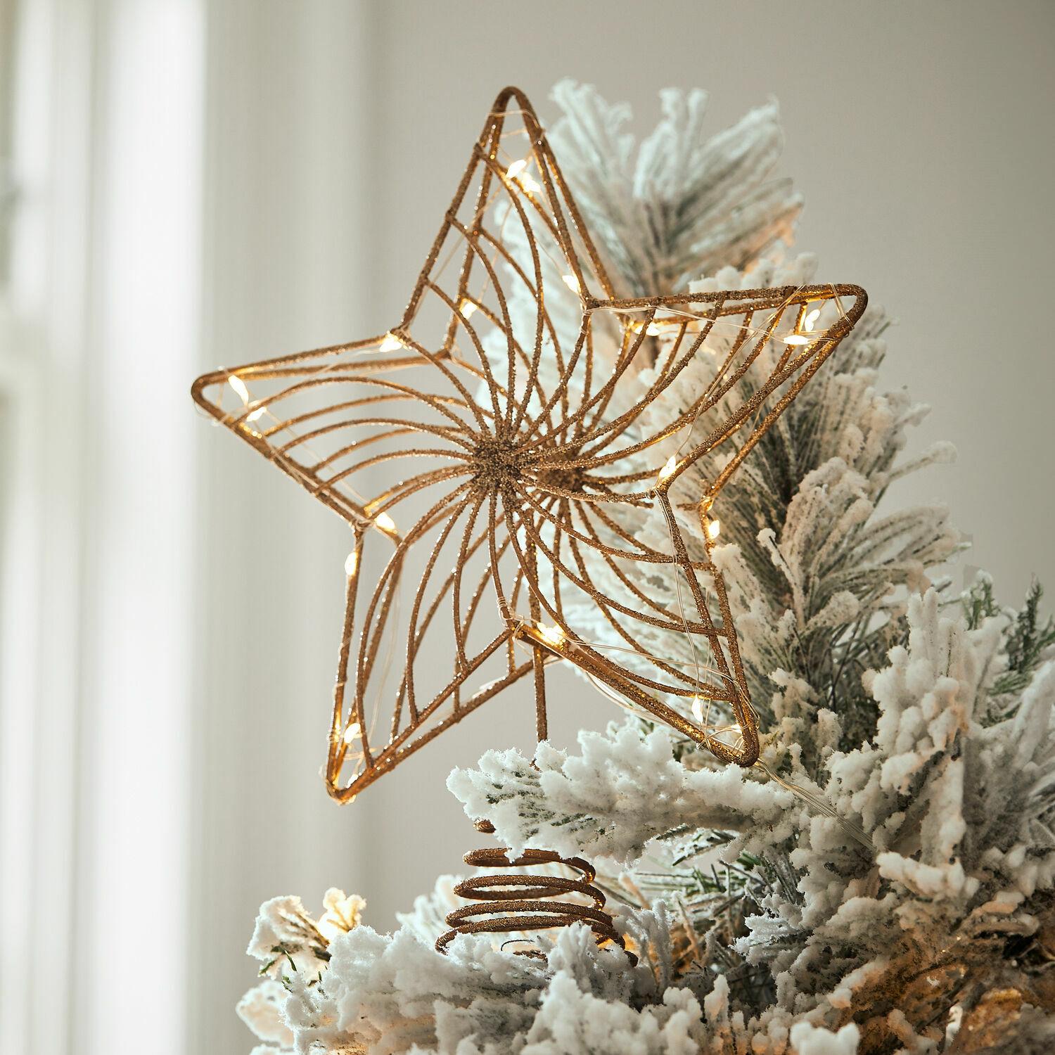 Goldene Metallstern mit LED-Lichtern auf schneebedecktem künstlichen Weihnachtsbaum als Baumspitze