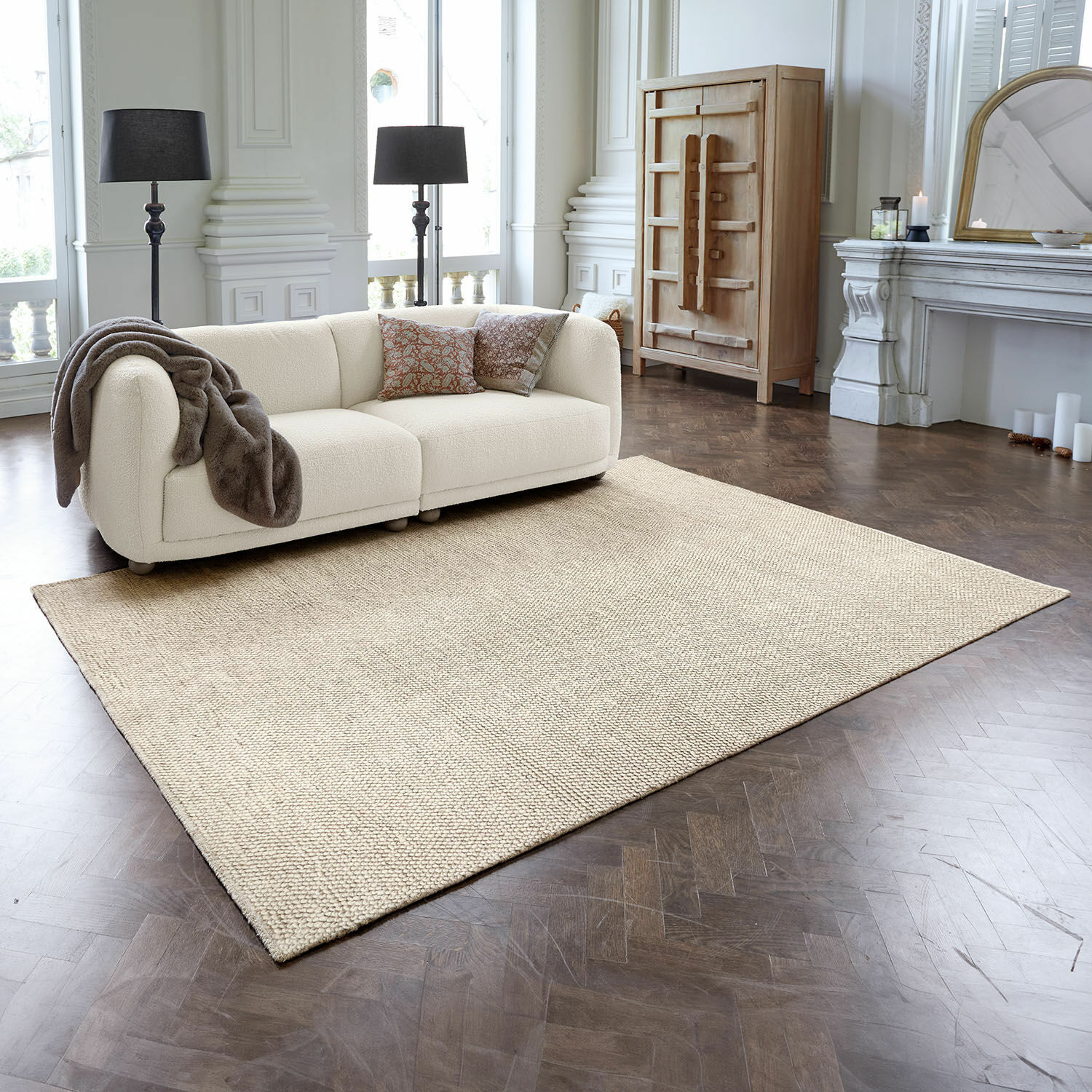 Teppich Coleman Beigefarbener Teppich aus Naturmaterial auf dunklem Holzboden in elegantem Wohnzimmer mit Sofa
