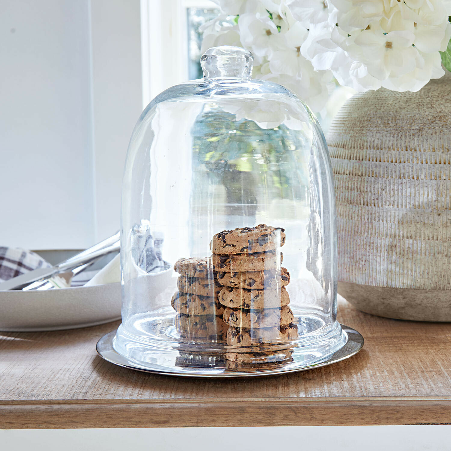 Glasglocke mit Metallboden auf Holztisch, gefüllt mit Schokoladenkeksen